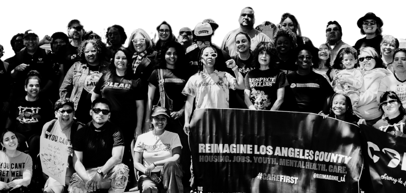 Group of diverse people holding a banner that reads 'Reimagine Los Angeles County' during a daytime outdoor event.
