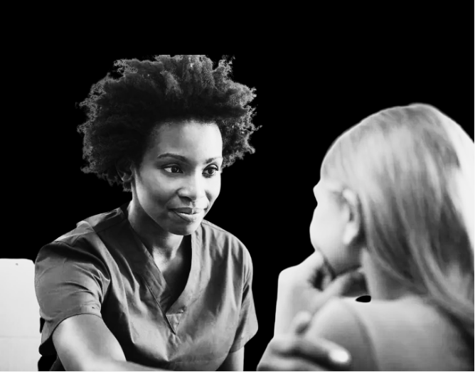 A woman in medical scrubs talking to a young girl with blonde hair, against a black background.