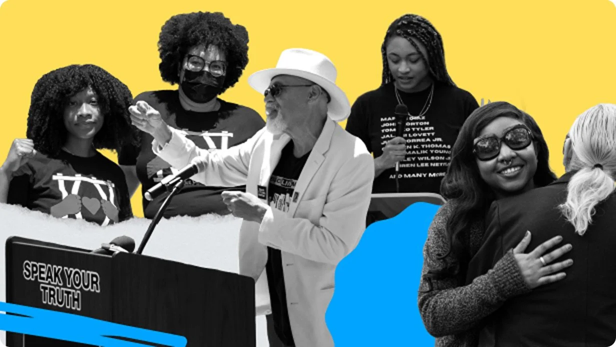 A group of seven diverse people at a public event, with some wearing black T-shirts, a man in a white blazer and hat speaking at a microphone, and others holding microphones or hugging, against a yellow background.