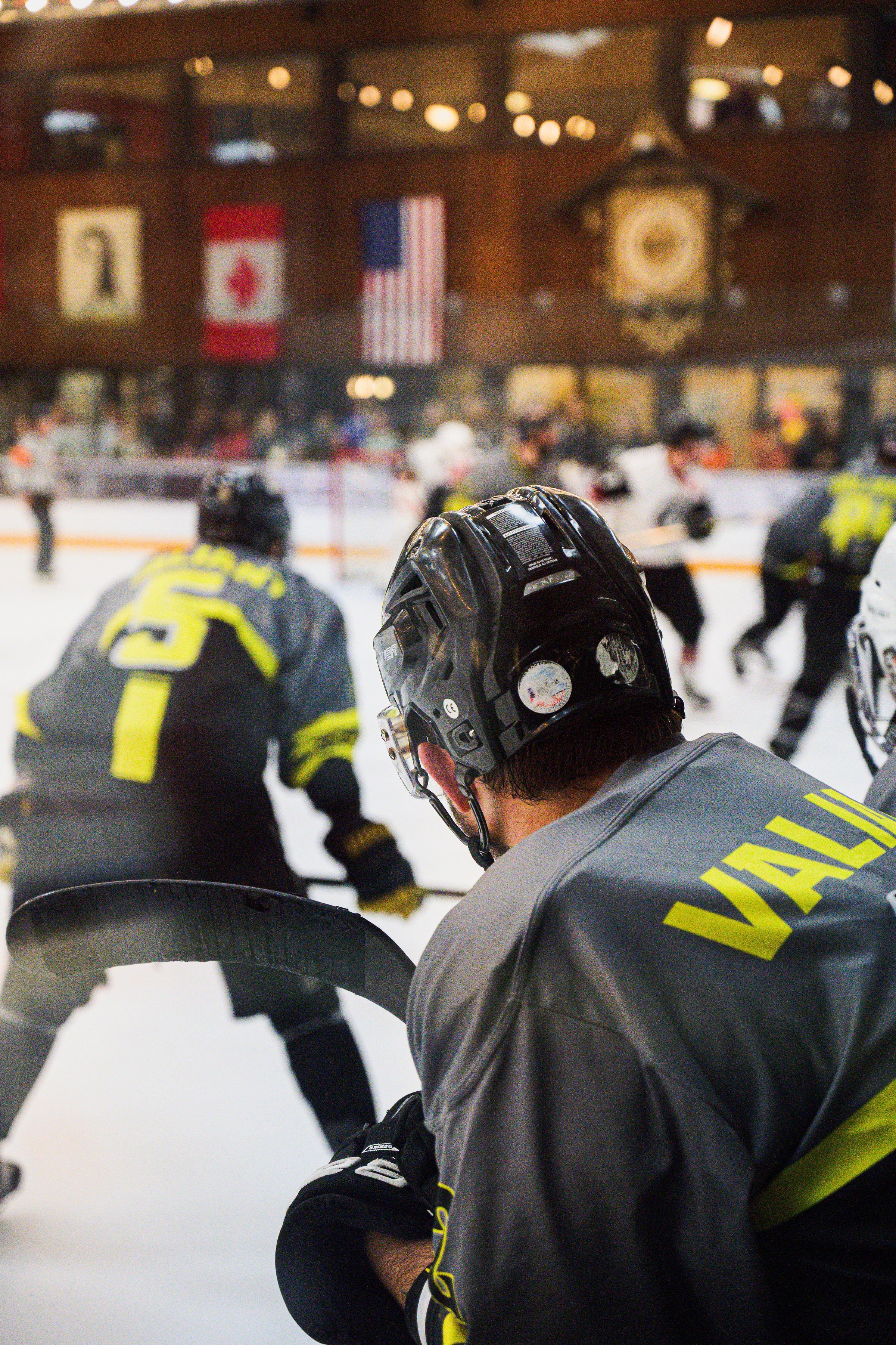 Hockey players practicing on indoor ice rink with American, Canadian, and Milwaukee flags hanging on wall.