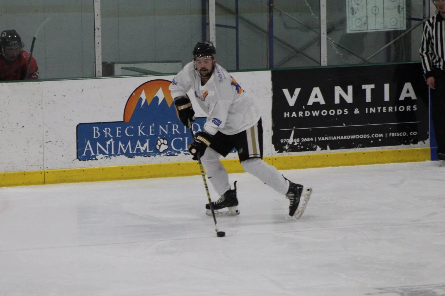 Hockey player in white jersey handling puck on ice rink with advertisements in background.