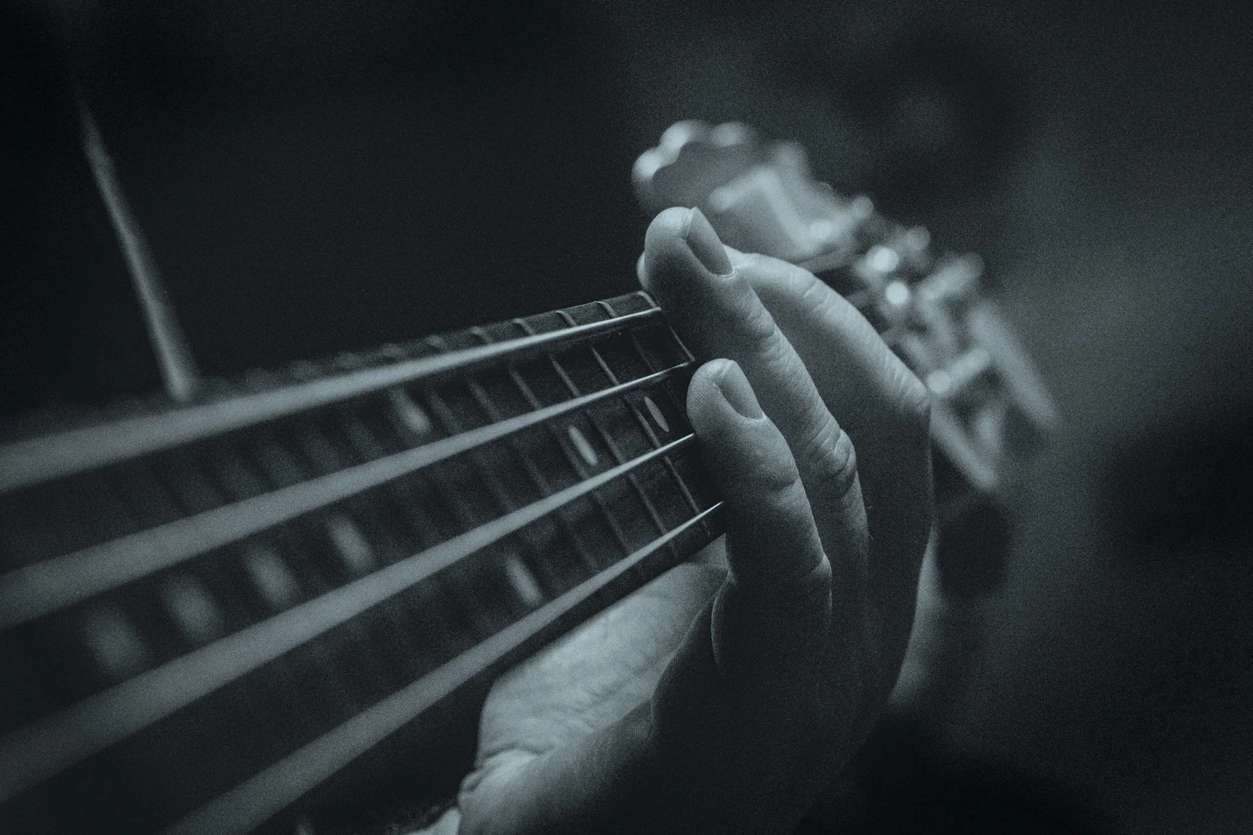 Close-up view of a person's hand playing an electric guitar, focusing on the fingers pressing the strings on the fretboard in black and white.