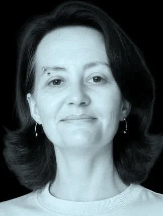 Black and white portrait of a woman with shoulder-length hair, wearing earrings and a light-colored top, looking at the camera with a neutral expression.