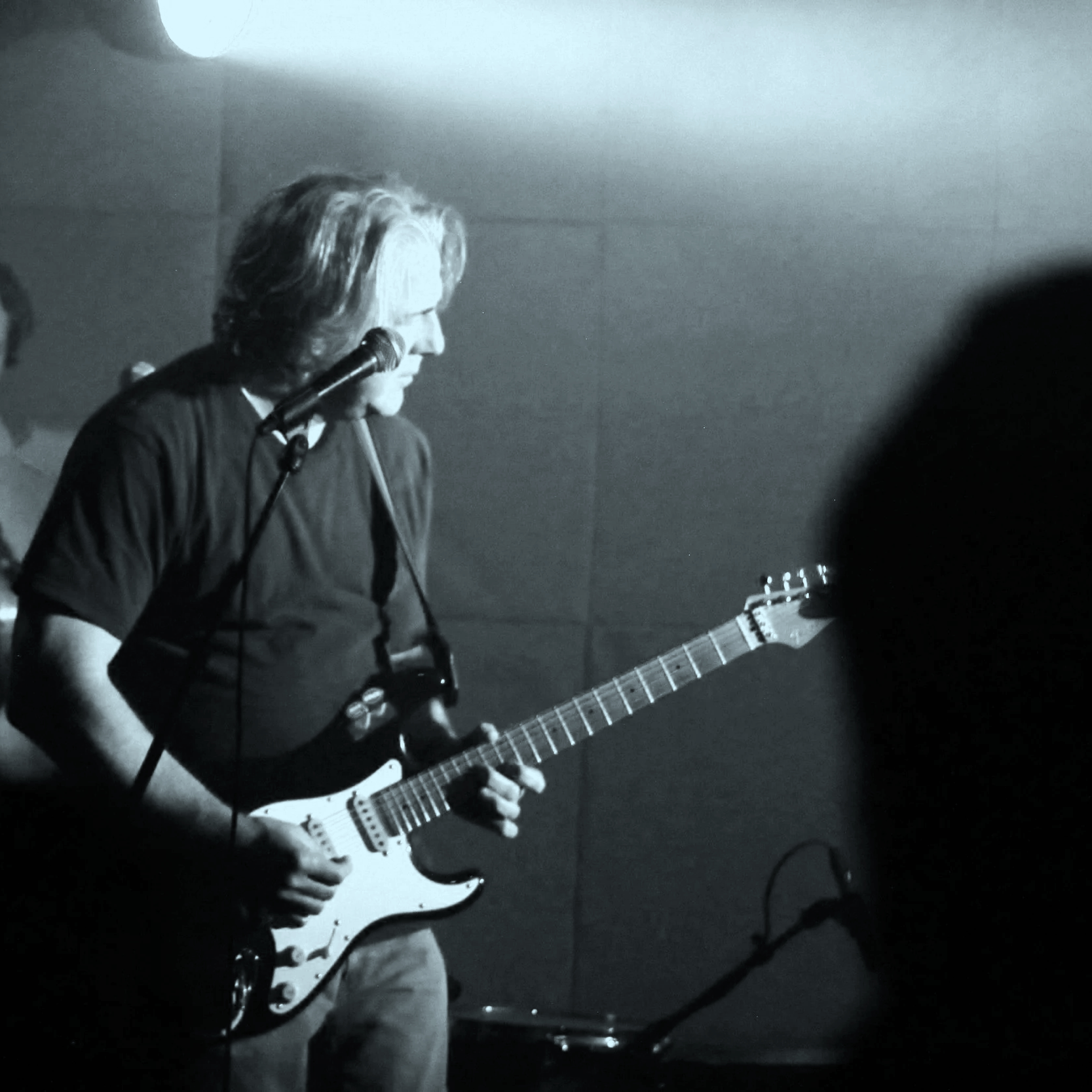 A person playing an electric guitar on stage in black and white.