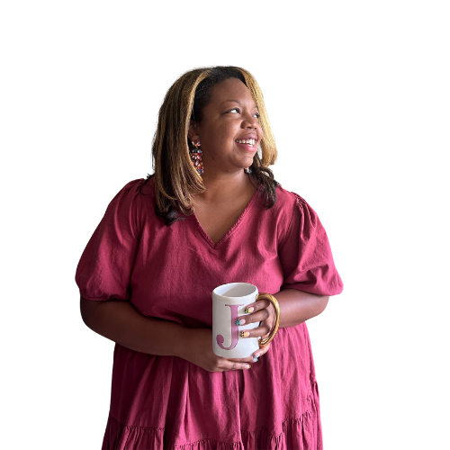 A smiling woman with shoulder-length hair, wearing a pink dress and large earrings, holding a coffee mug with a letter J on it, against a black background.