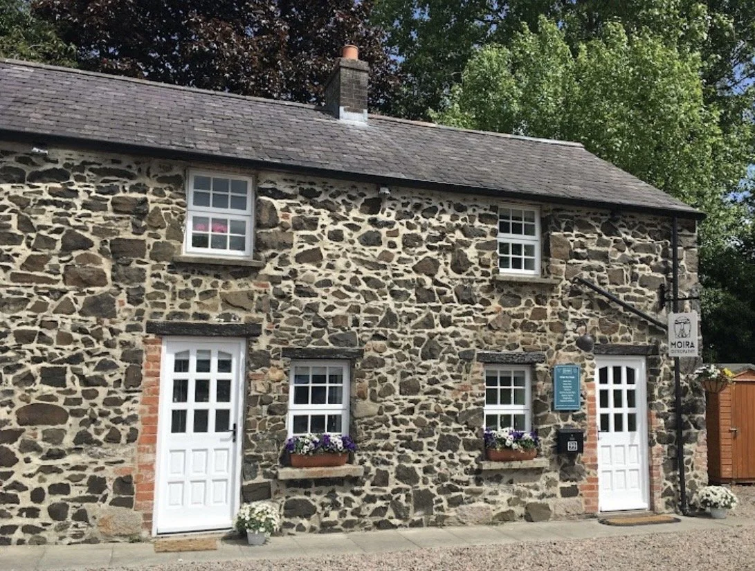 Moira Counselling Practice's office in Moira. A private, stone cottage with white doors and windows, flower boxes, and a sign for Moira Osteopathy.