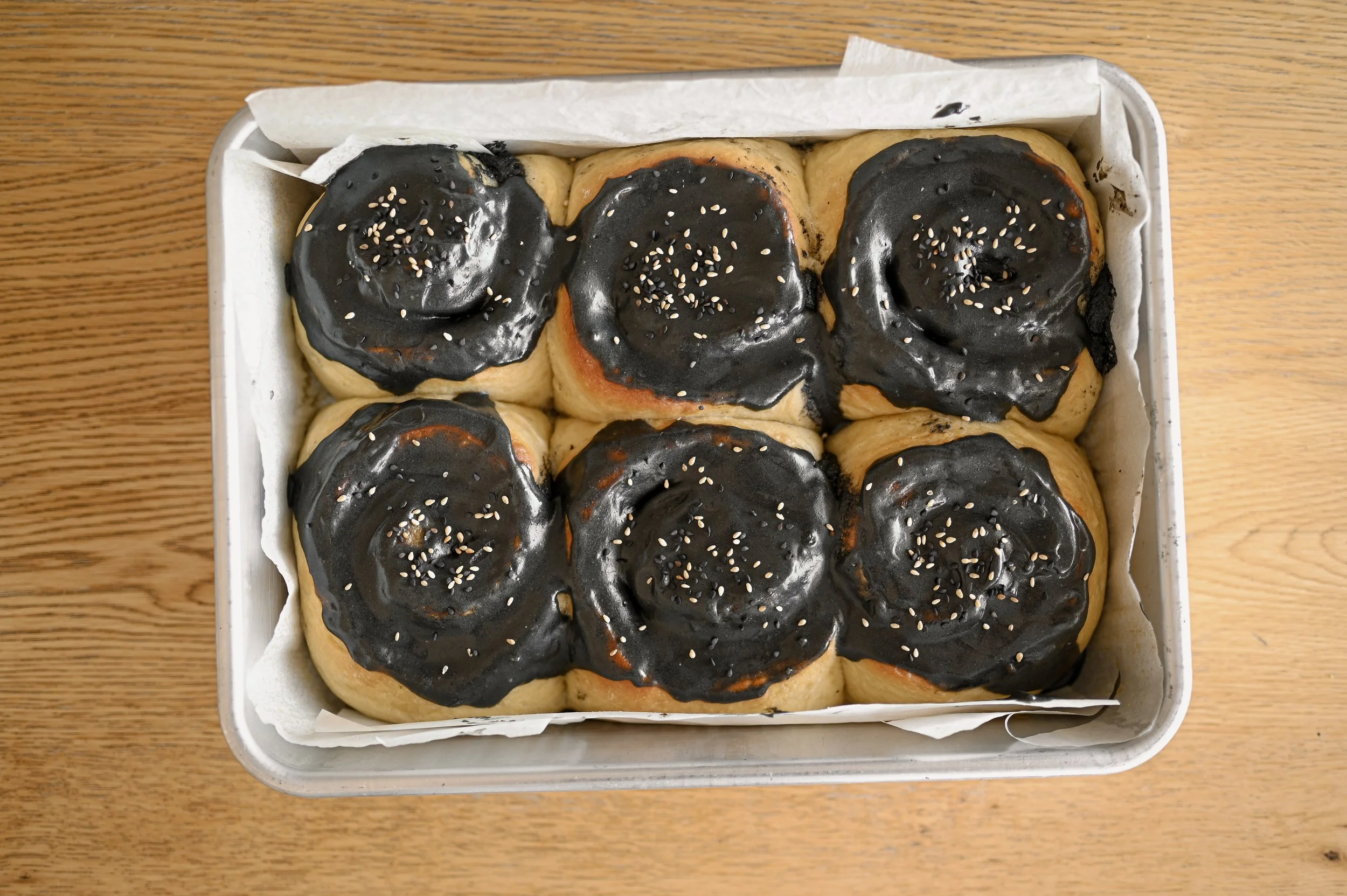Tray of six black sesame rolls topped with black sesame buttercream and black and white sesame seeds.