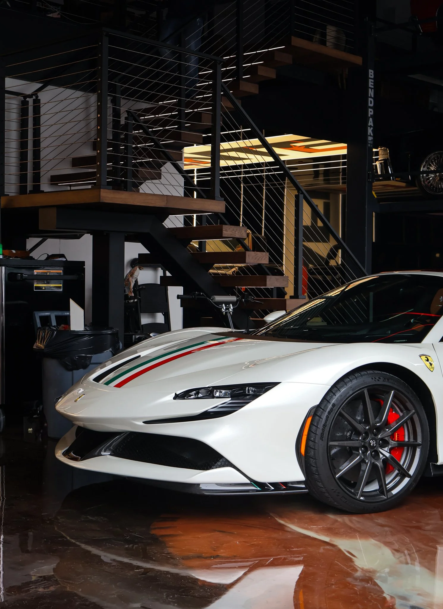 White Ferrari with Italian flag stripe parked indoors near a staircase and storage area.