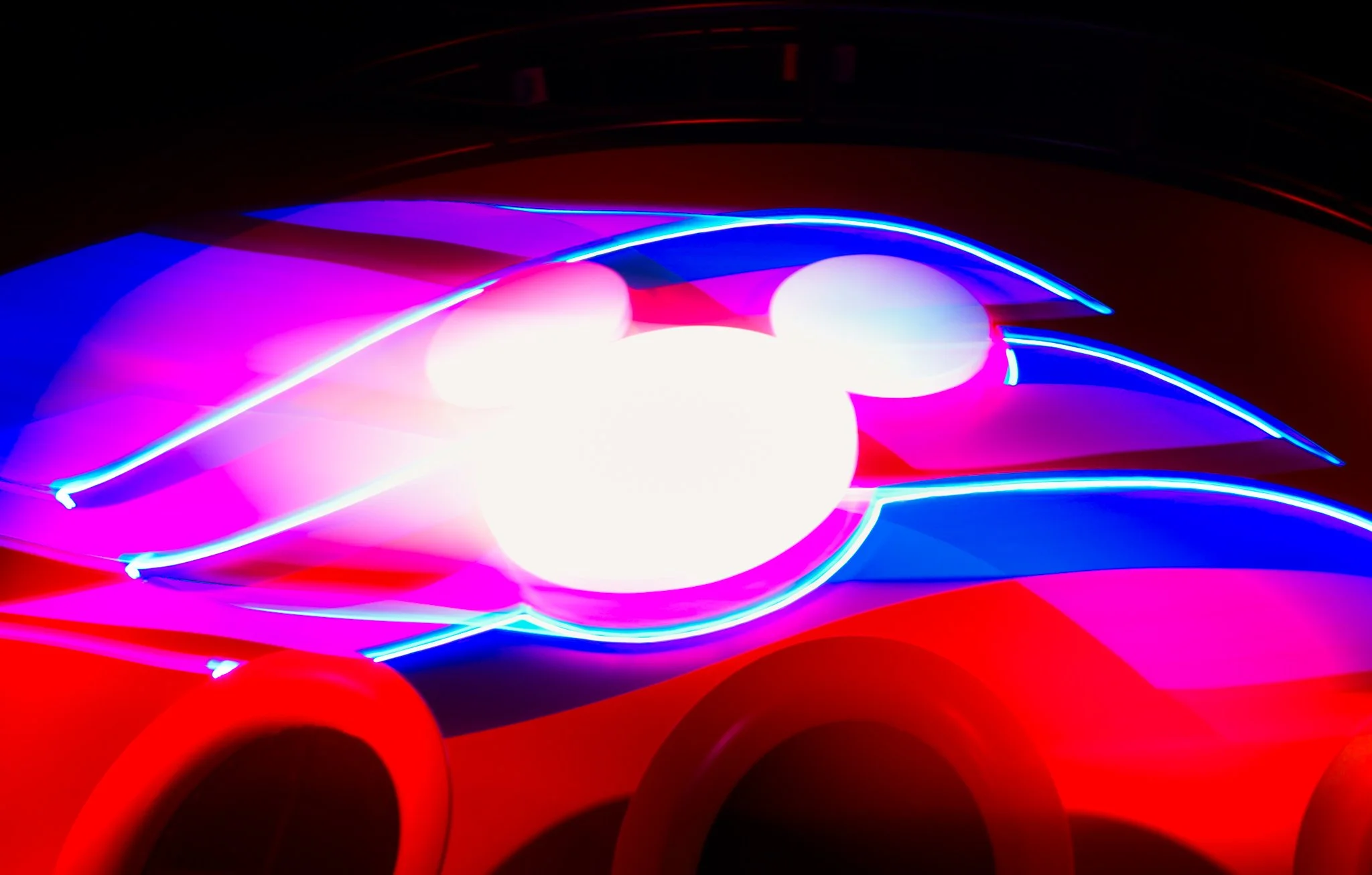 Close-up of a brightly glowing LED headlight on a red vehicle with vibrant blue, pink, and purple neon illumination.