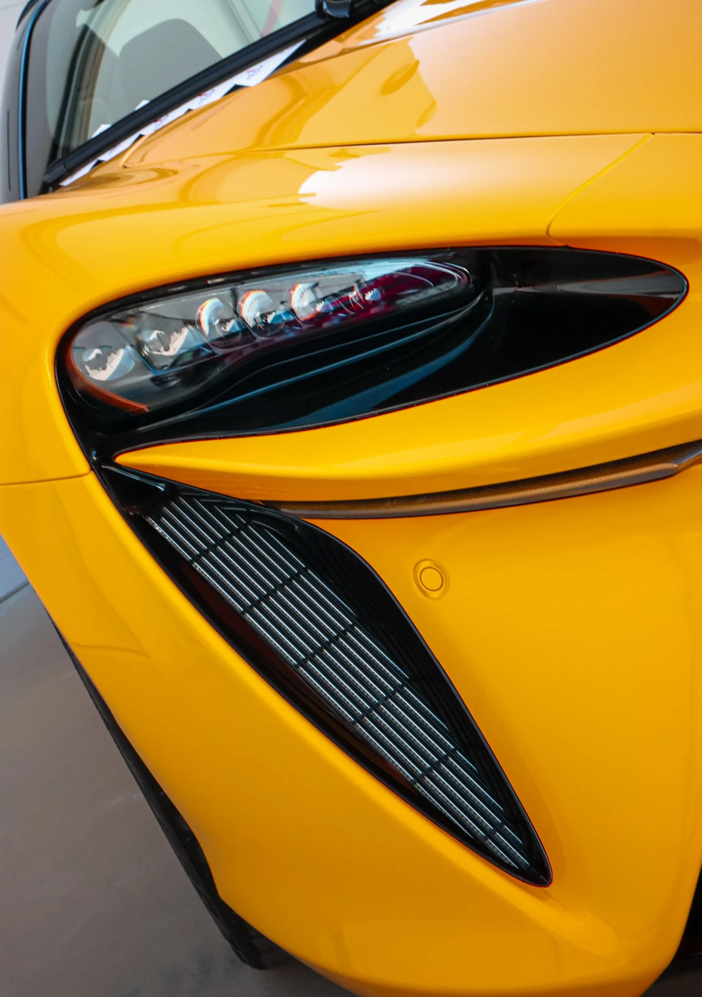 Close-up of the front left side of a yellow sports car, showing the headlight and part of the front grille.