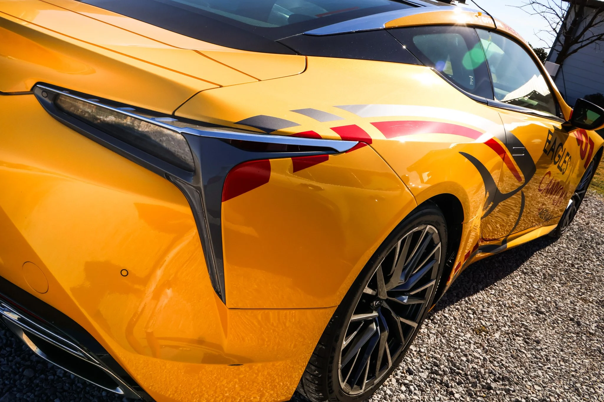 Yellow sports car with a racing decal design, featuring black and red accents, parked on gravel.