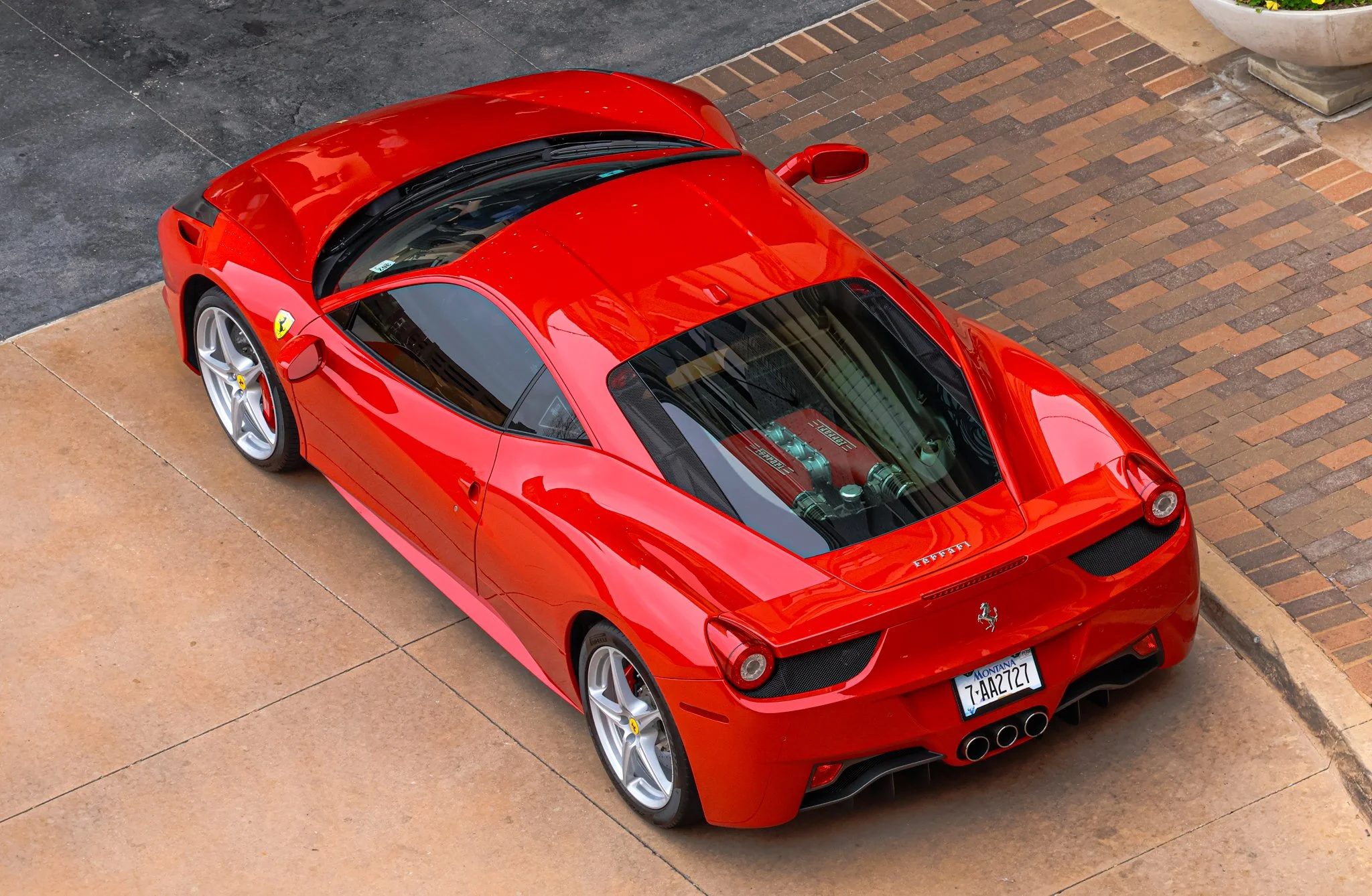 Red Ferrari sports car parked on a concrete and brick driveway, viewed from above.