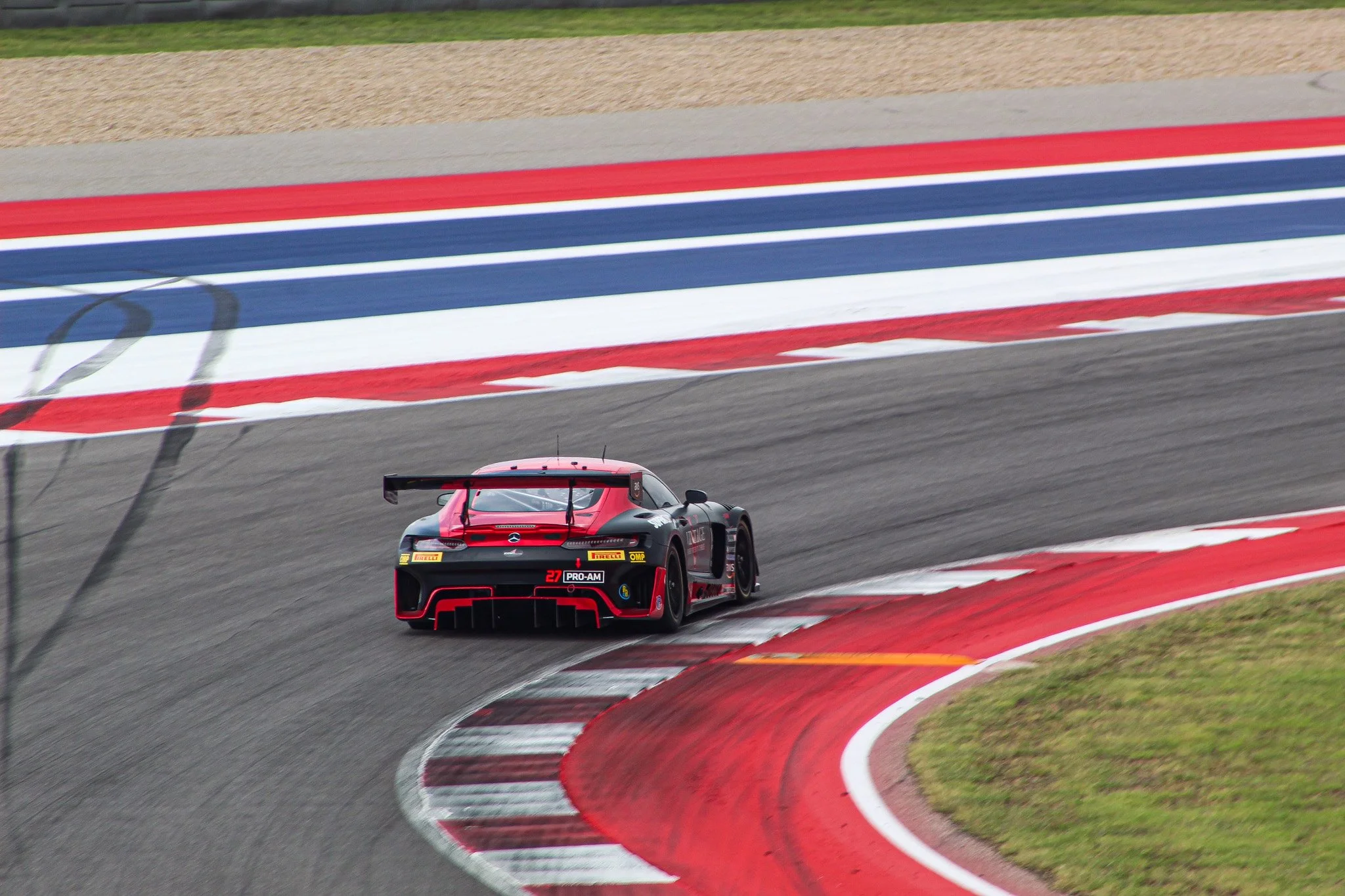 A black and red race car with a large rear wing driving on a race track with red, white, and blue curbing.