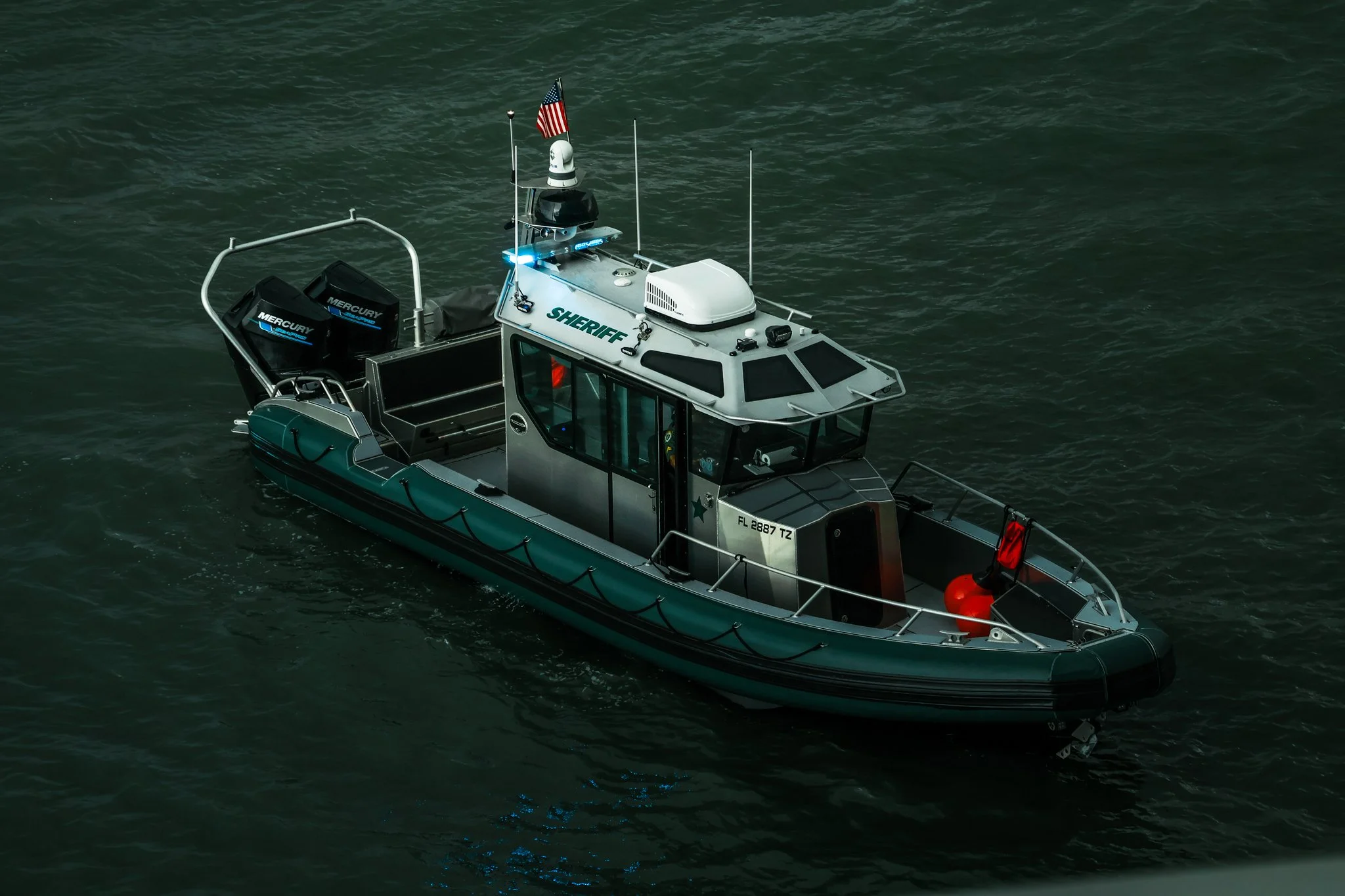 A Sheriff's patrol boat on water with two Mercury outboard motors, an American flag, and a red rescue buoy.