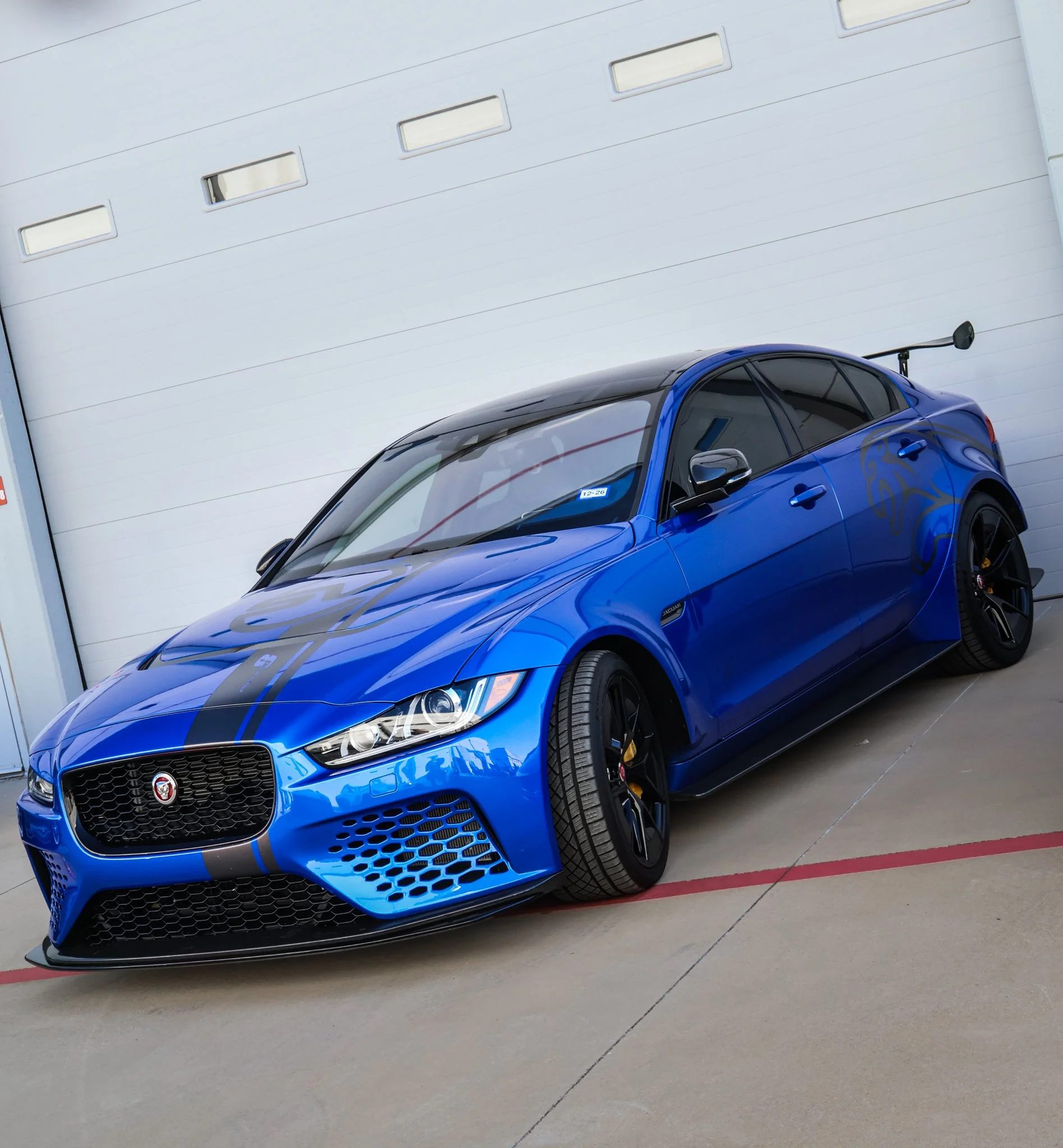 A blue sports car with black racing stripes parked in front of a garage door.