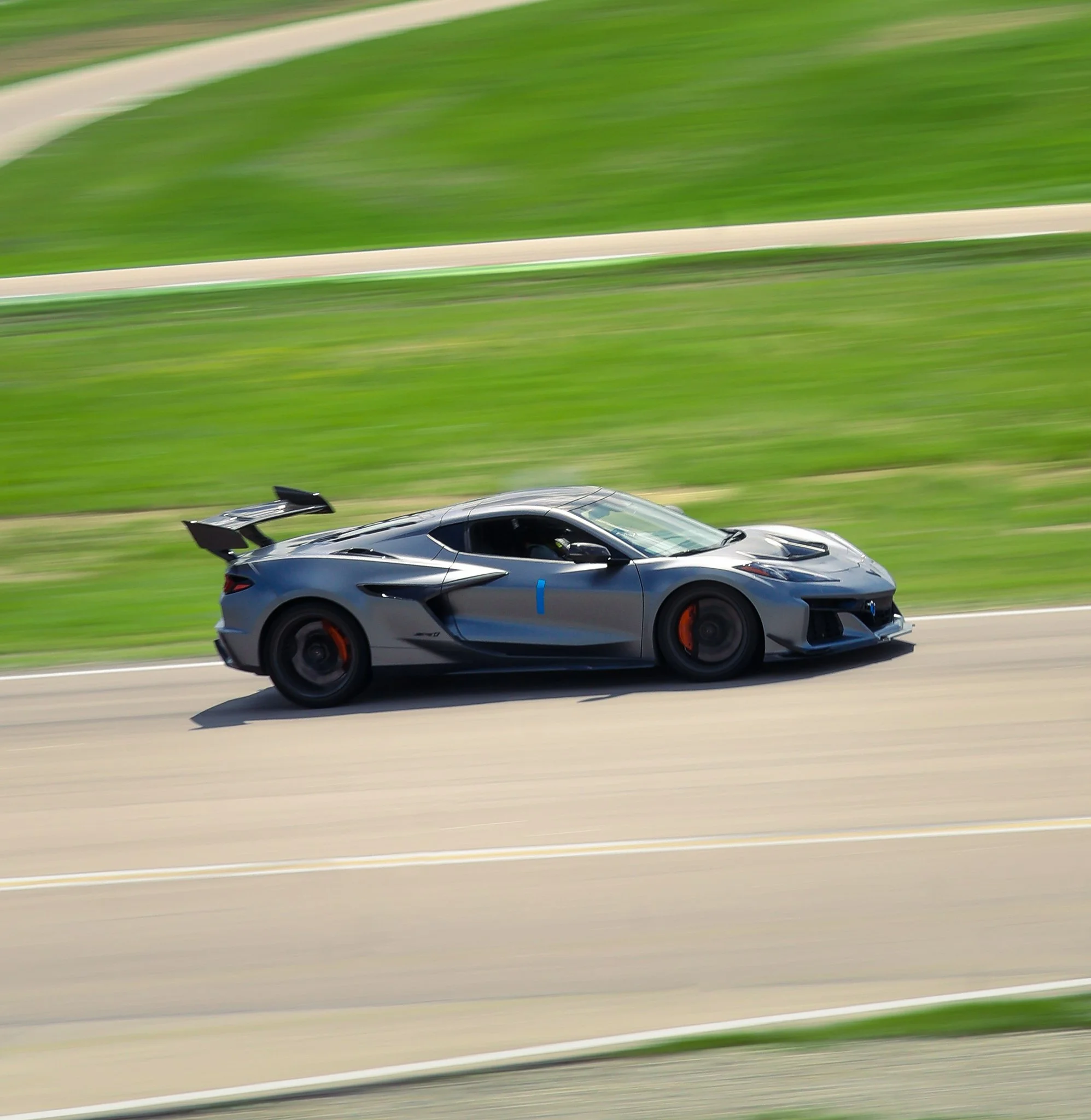 A gray sports car racing on a track with green grass background, featuring aerodynamic design and large rear wing.