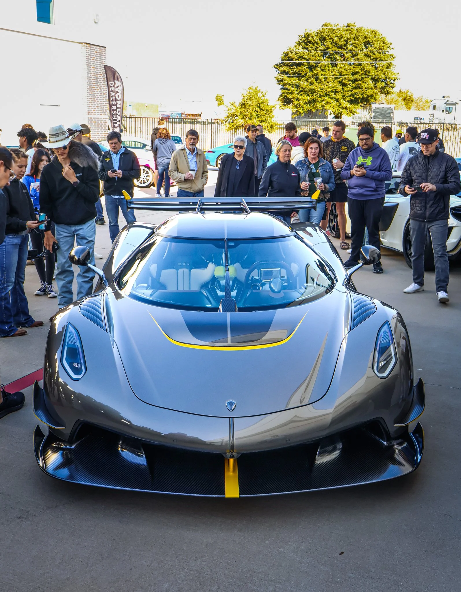 A sleek, black sports car with yellow accents displayed outdoors with a crowd of people gathered around it at a car show.