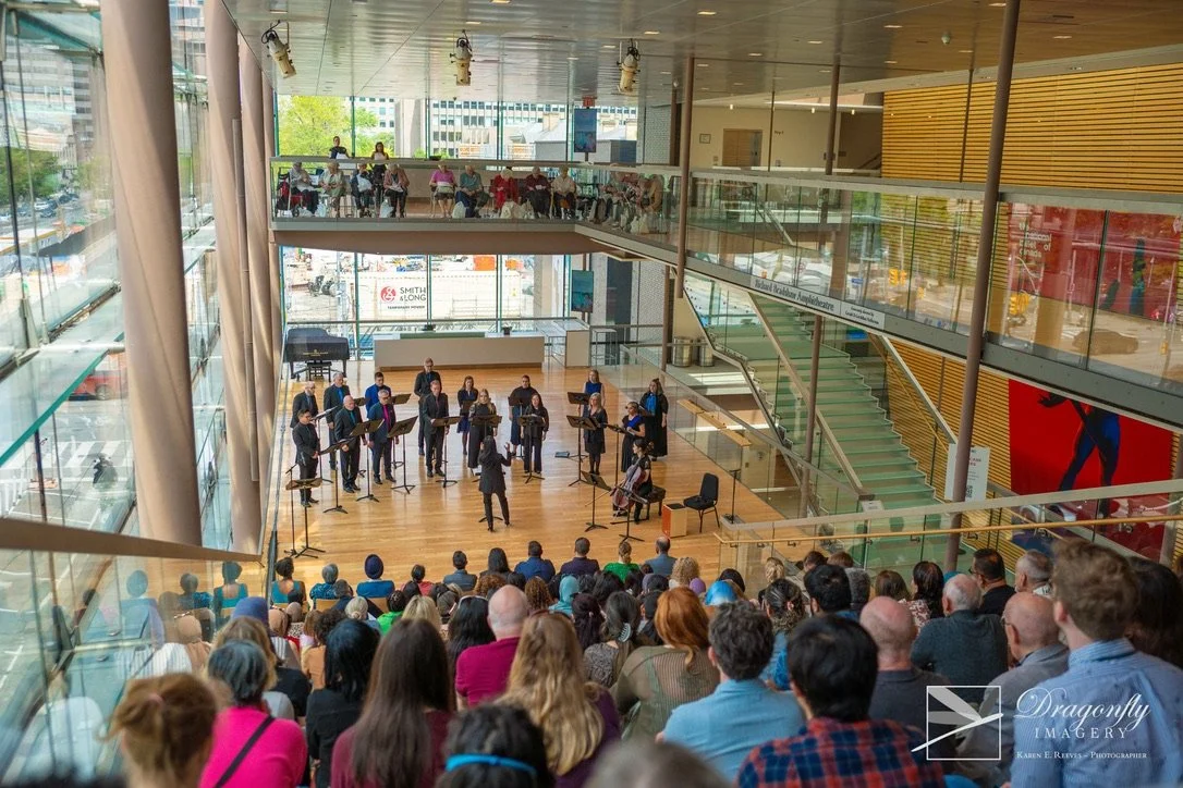A musical concert taking place indoors with an audience watching a group of musicians and a conductor on stage.