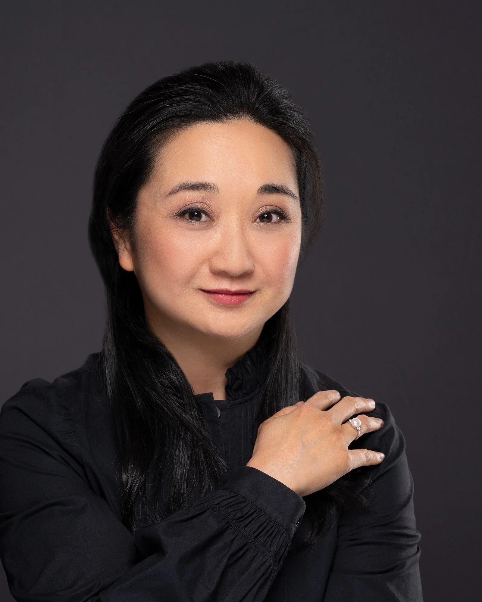 Portrait of a Cheryll Cheung with dark hair wearing a black jacket, posing against a dark background.