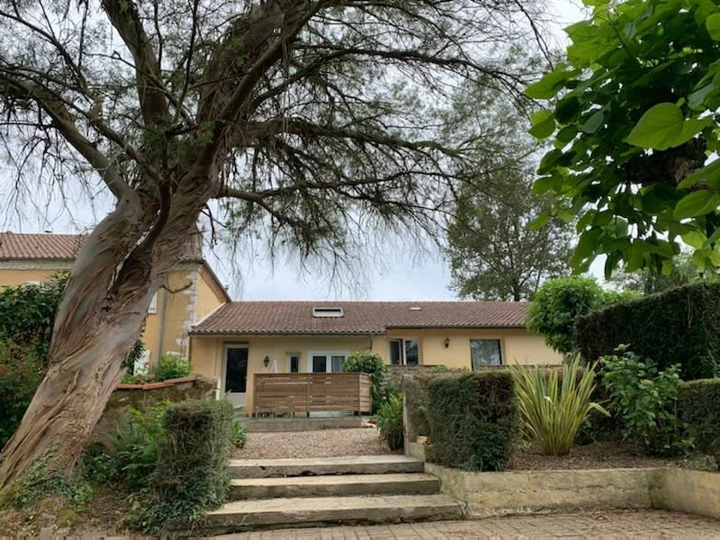Maison avec jardin, arbres et escalier en pierre devant la maison.