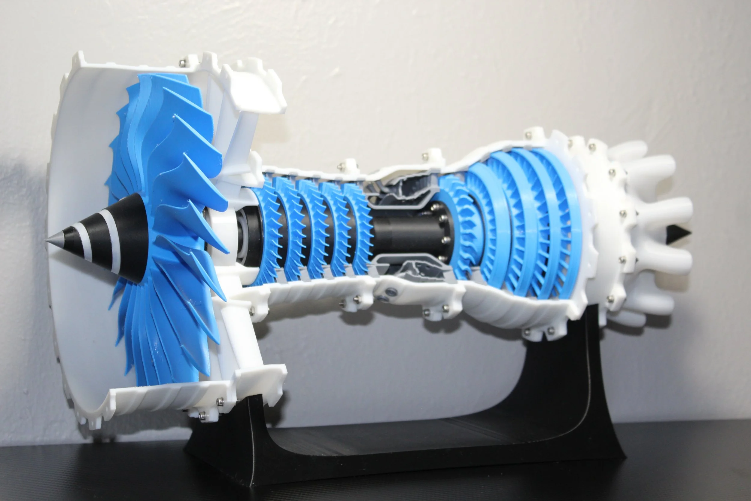 Cross-sectional model of a jet engine showing internal components like the turbines, compressors, and combustion chamber, with blue and white parts.