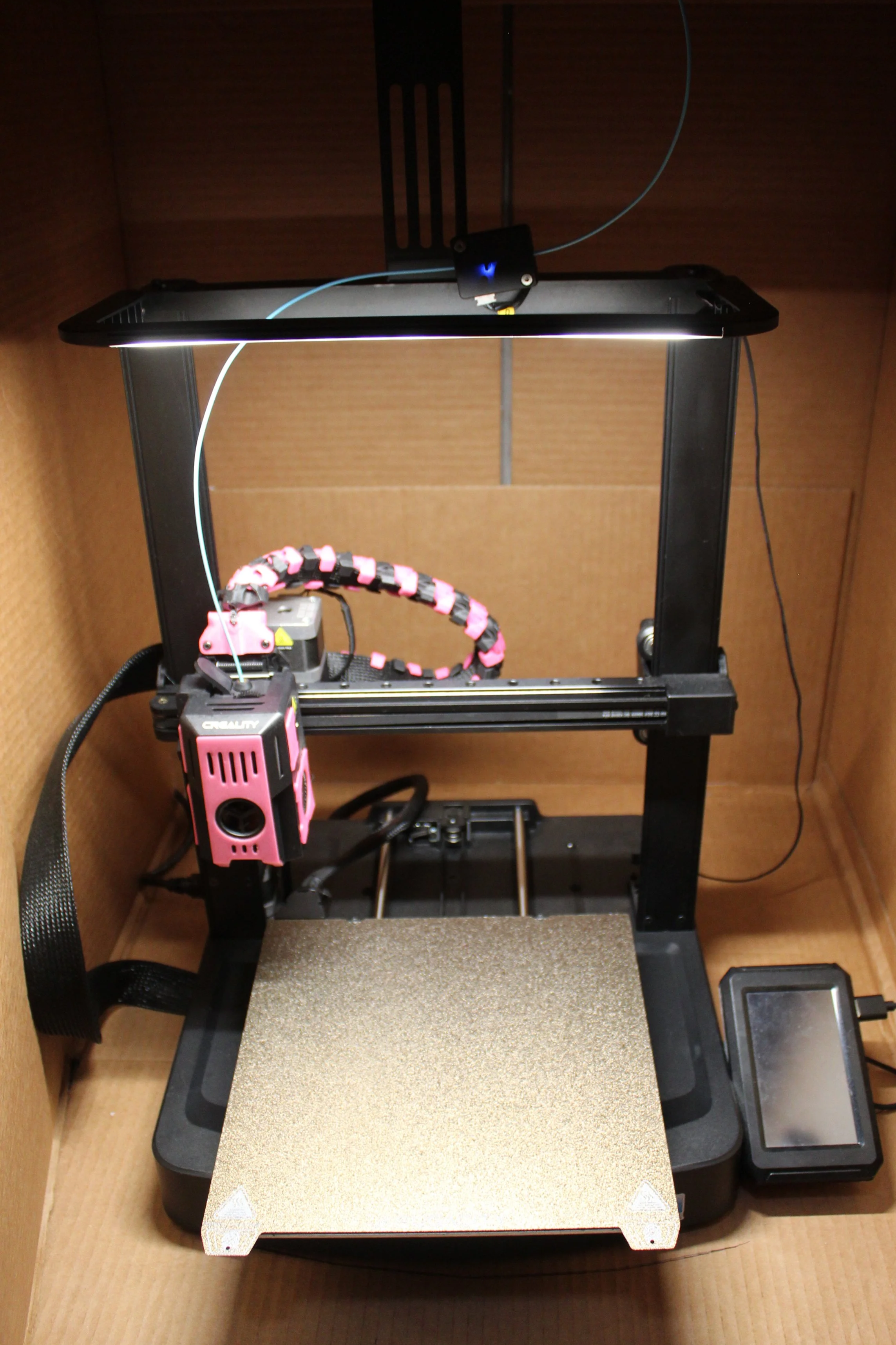 A 3D printer in a cardboard enclosure, ready for printing.