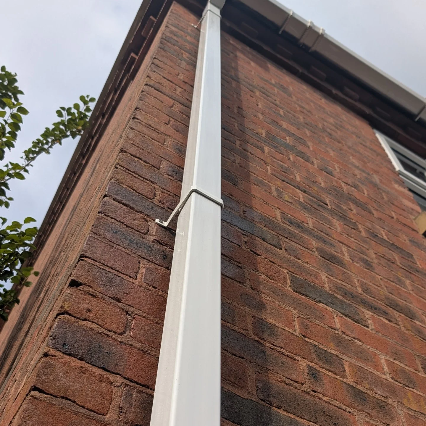 Close-up of a brick house corner with a vertical white rain gutter attached.