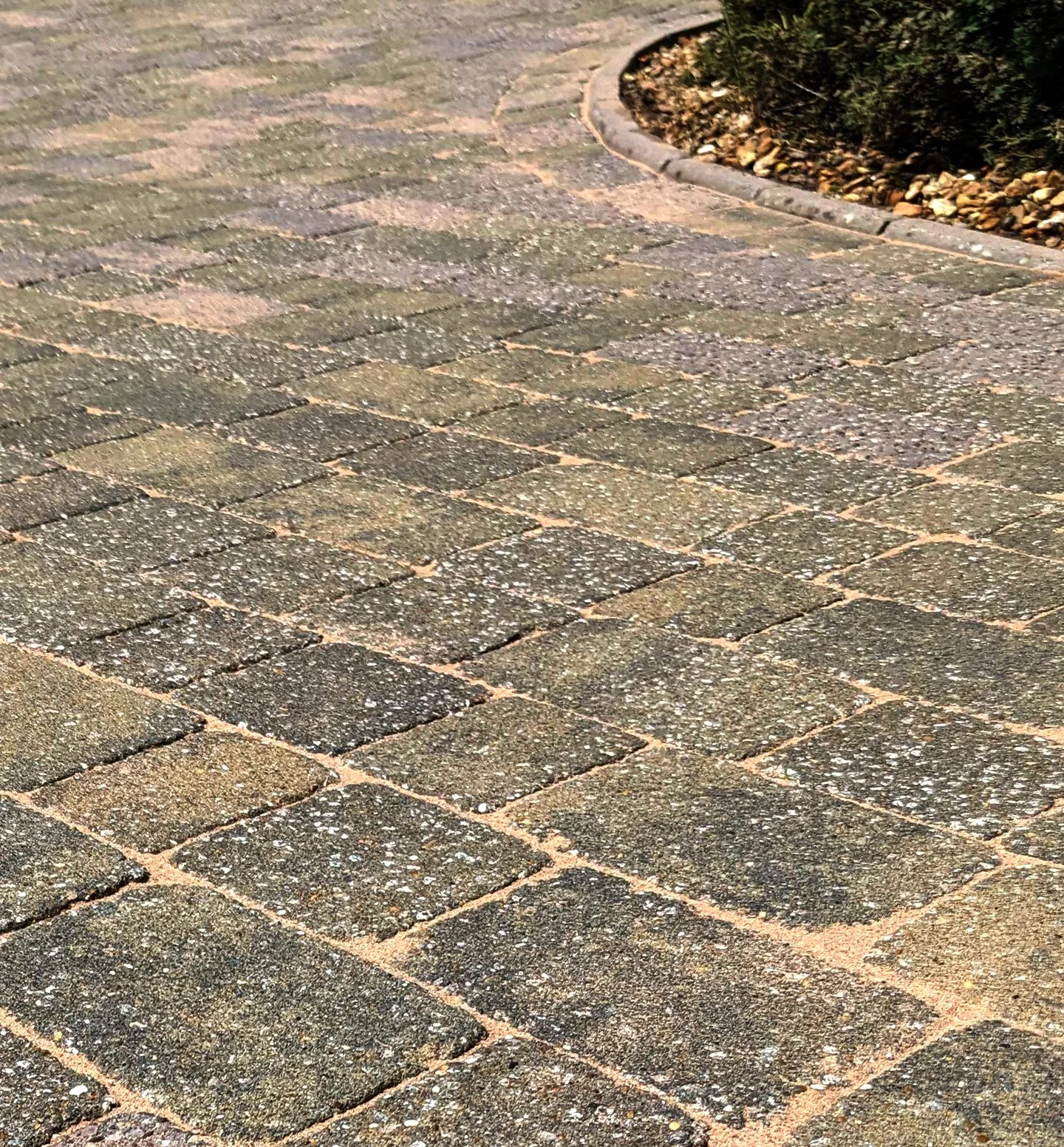 Close-up view of a paved brick pathway with a curved edge and a garden bed with small rocks and shrubs.