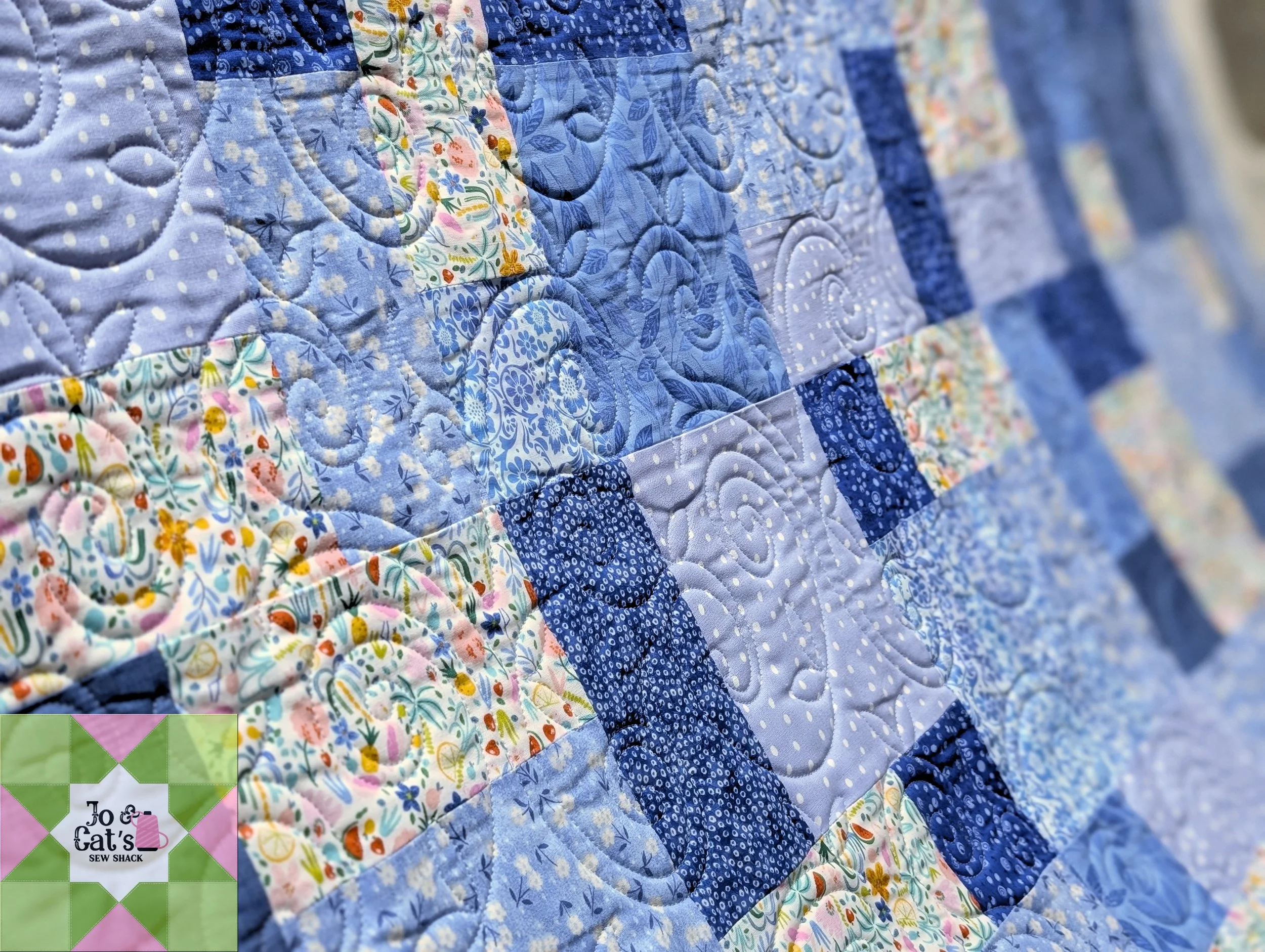 Close-up of a patchwork quilt with various blue, white, and pastel floral and dotted fabric pieces.