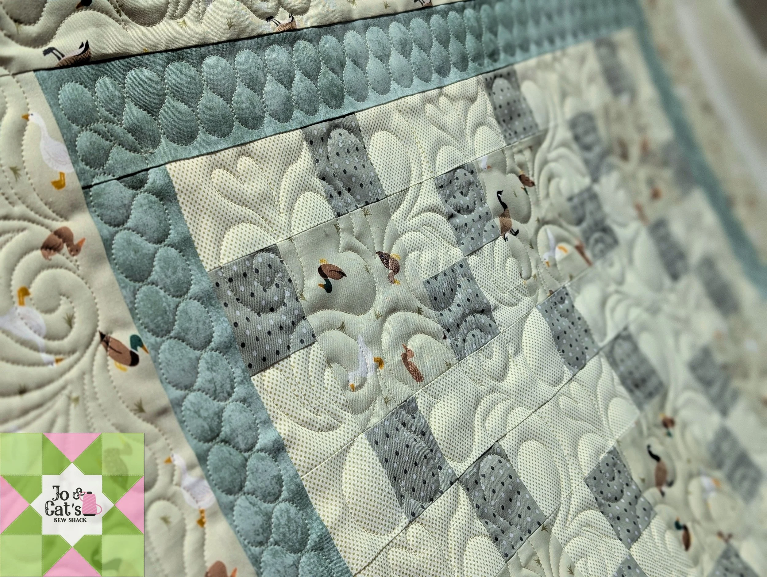 Close-up image of a quilt with animal and nature print, featuring various swan and duck designs, stitched patterns, and a decorative border.