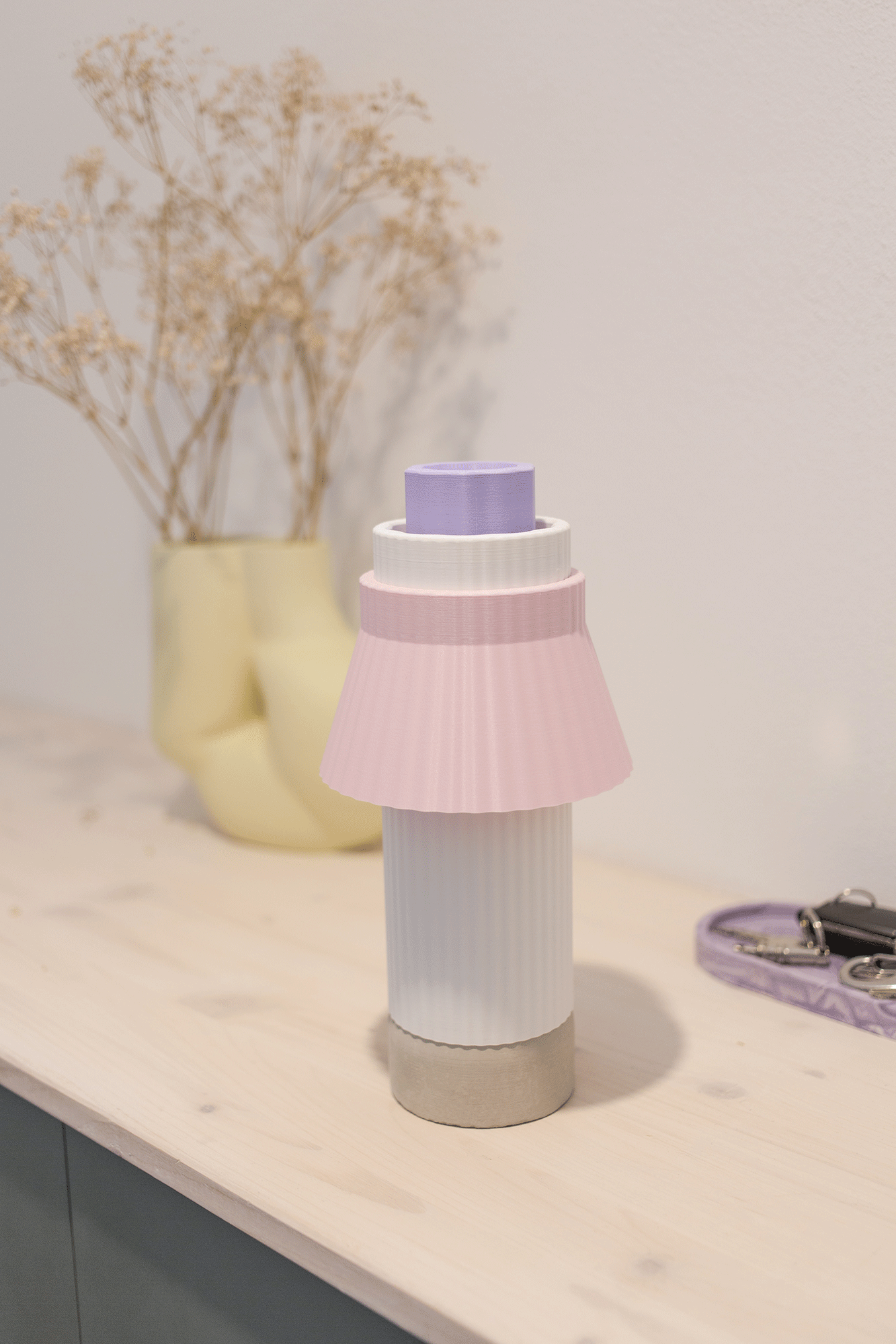 Kunstvolle Kerzen in pastellfarben, auf einem Tisch mit einer Vase mit getrockneten Blumen im Hintergrund.