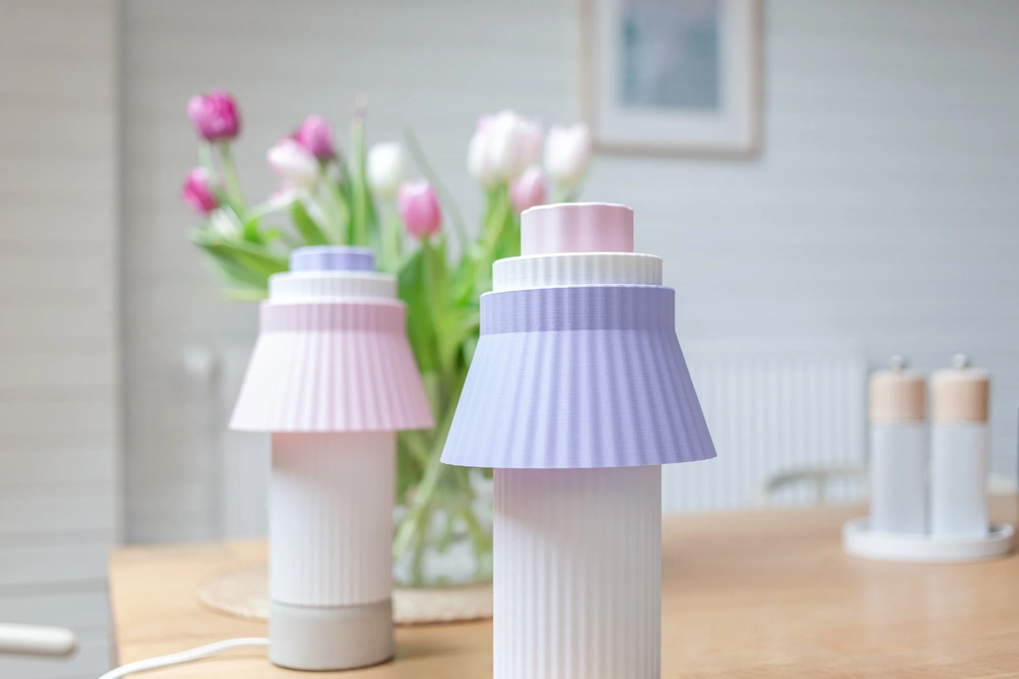 Vase mit Tulpen und zwei dekorative Lampen im pastelfarbenen Design auf einem Holztisch.