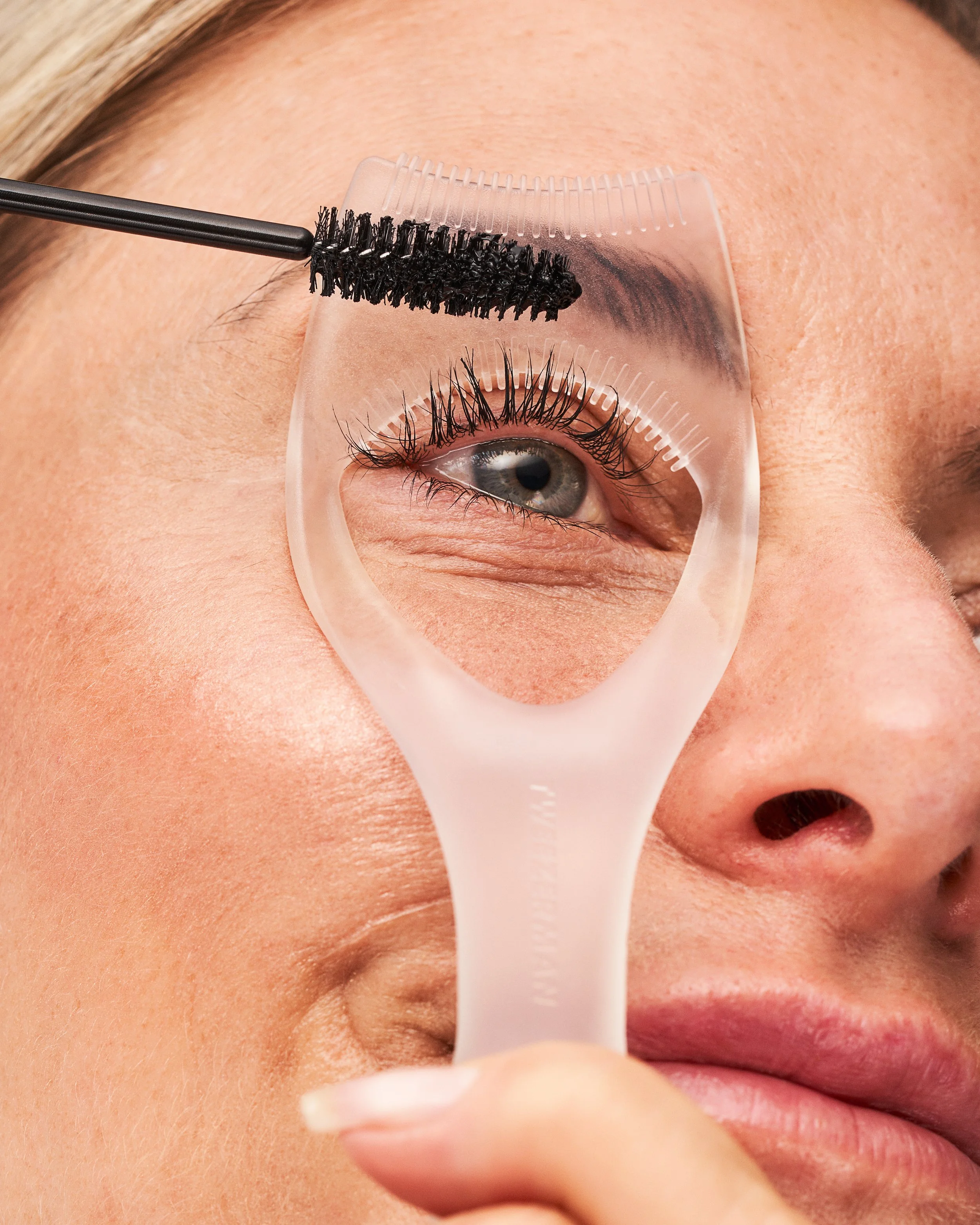 Older white model using an eye guard tool whilst applying mascara.