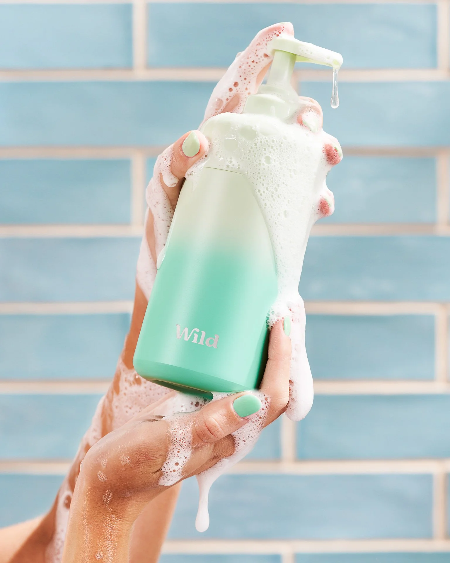 The model's hand is holding a green ombre shower gel bottle, while covered in dripping suds.
