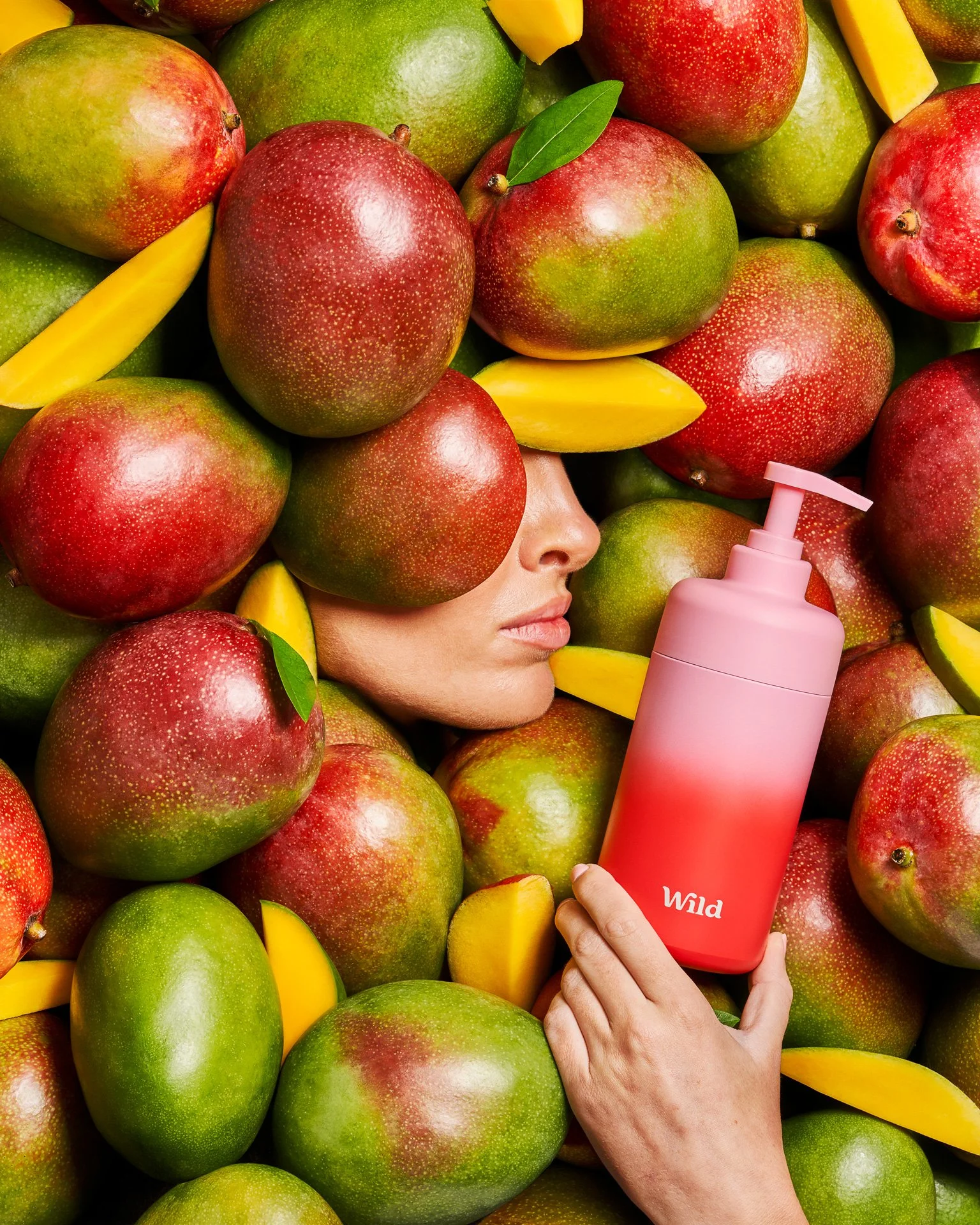 Model's face buried in fresh cut mangoes, with only her nose and mouth poking through, whilst holding a red and pink shoer gel bottle.