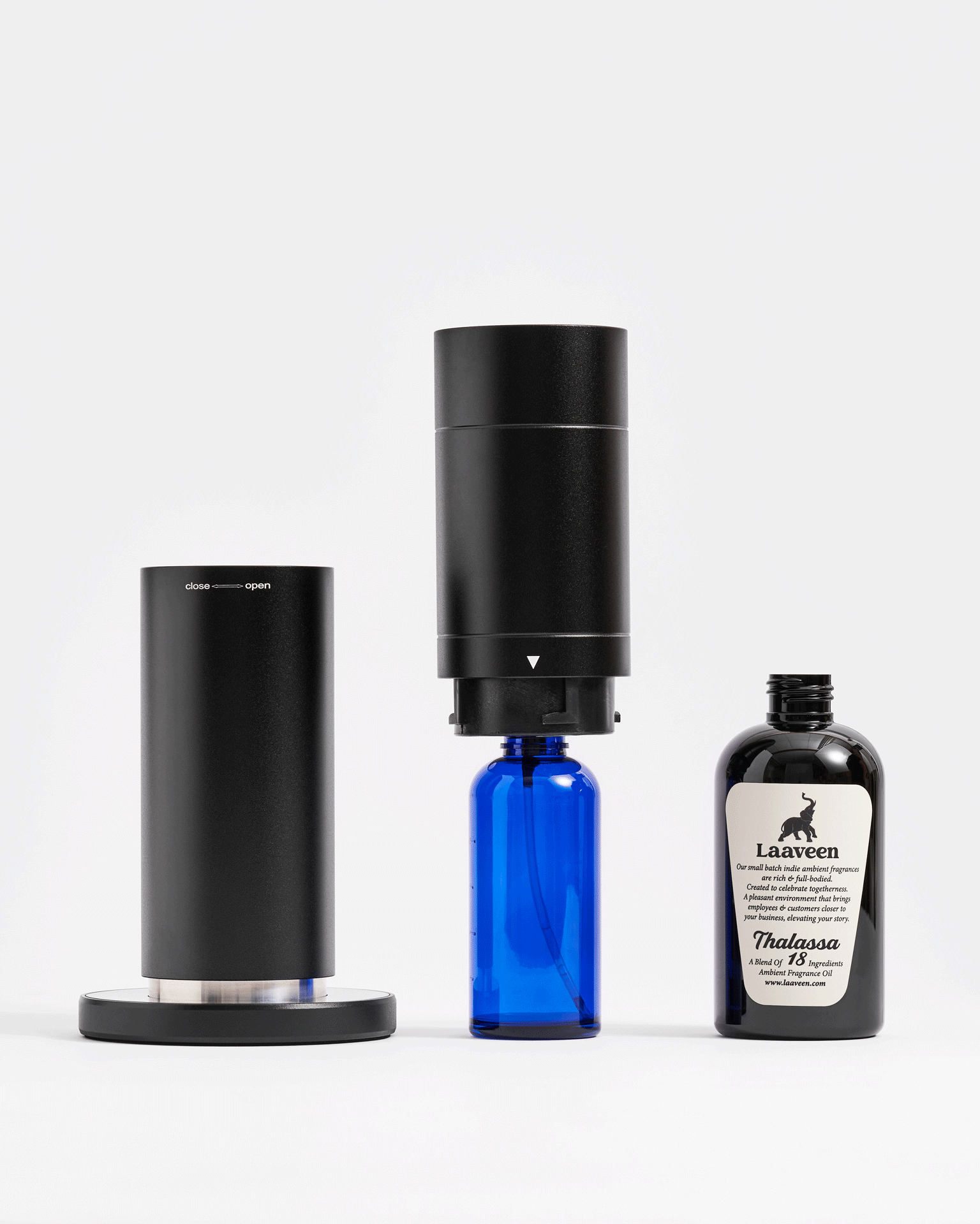 Black essential oil diffuser with a blue glass bottle attached and a black bottle of Laaven Thalassa ambiance fragrance oil beside it on a white background.