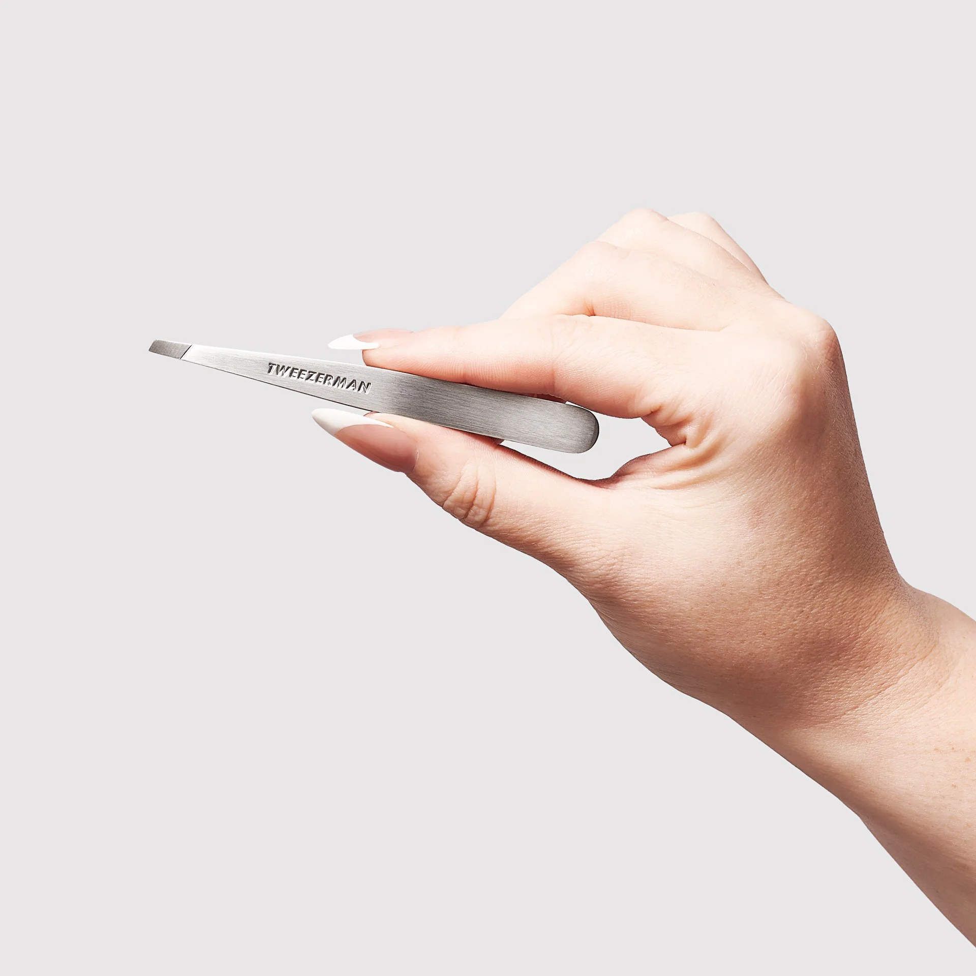 Hand holding a silver tweezers from Tweezerman.