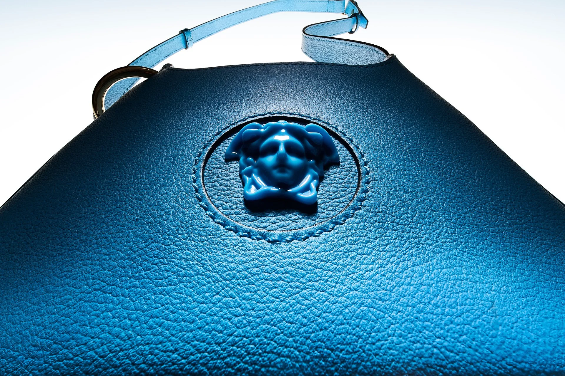 Close-up of a blue leather handbag with a Medusa head emblem on the front.