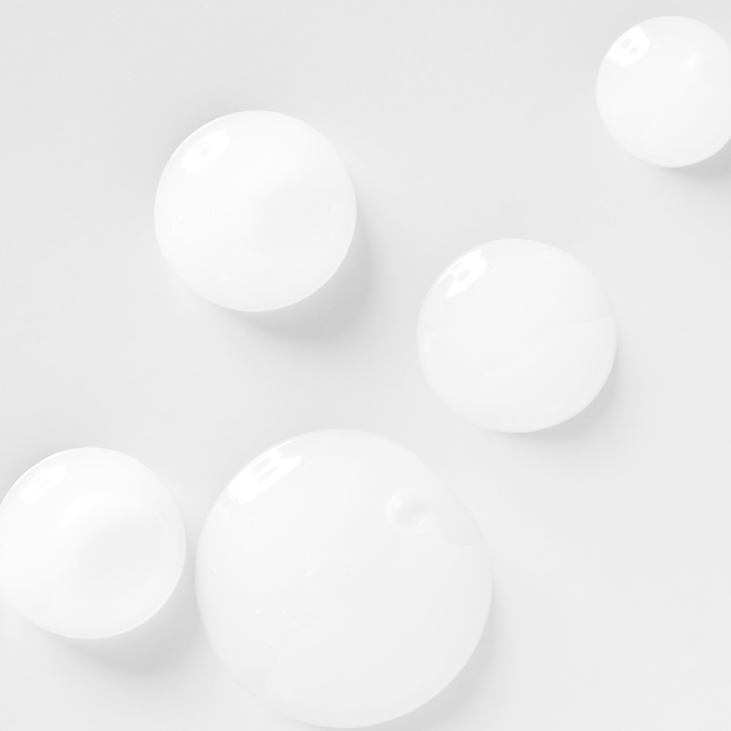 Several white spherical objects, possibly balls or bubbles, on a white surface.