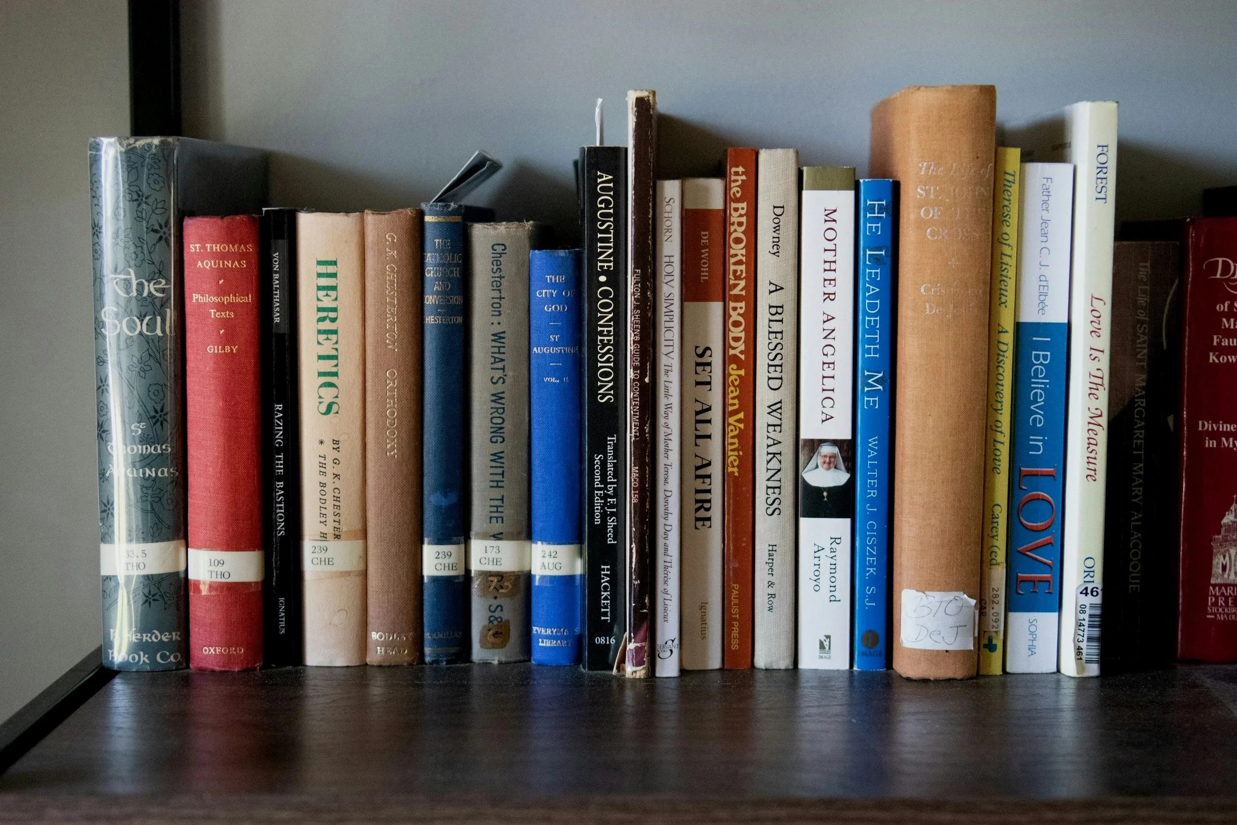 A row of books on a dark wooden shelf, featuring titles on religion, theology, and spirituality, with some books stacked vertically.