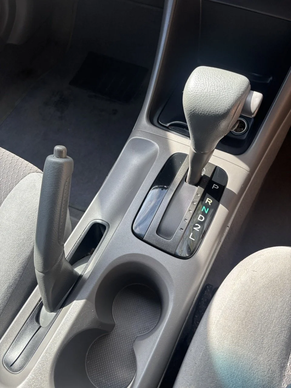 Central console of a car showing gear shift, handbrake, and cup holder.