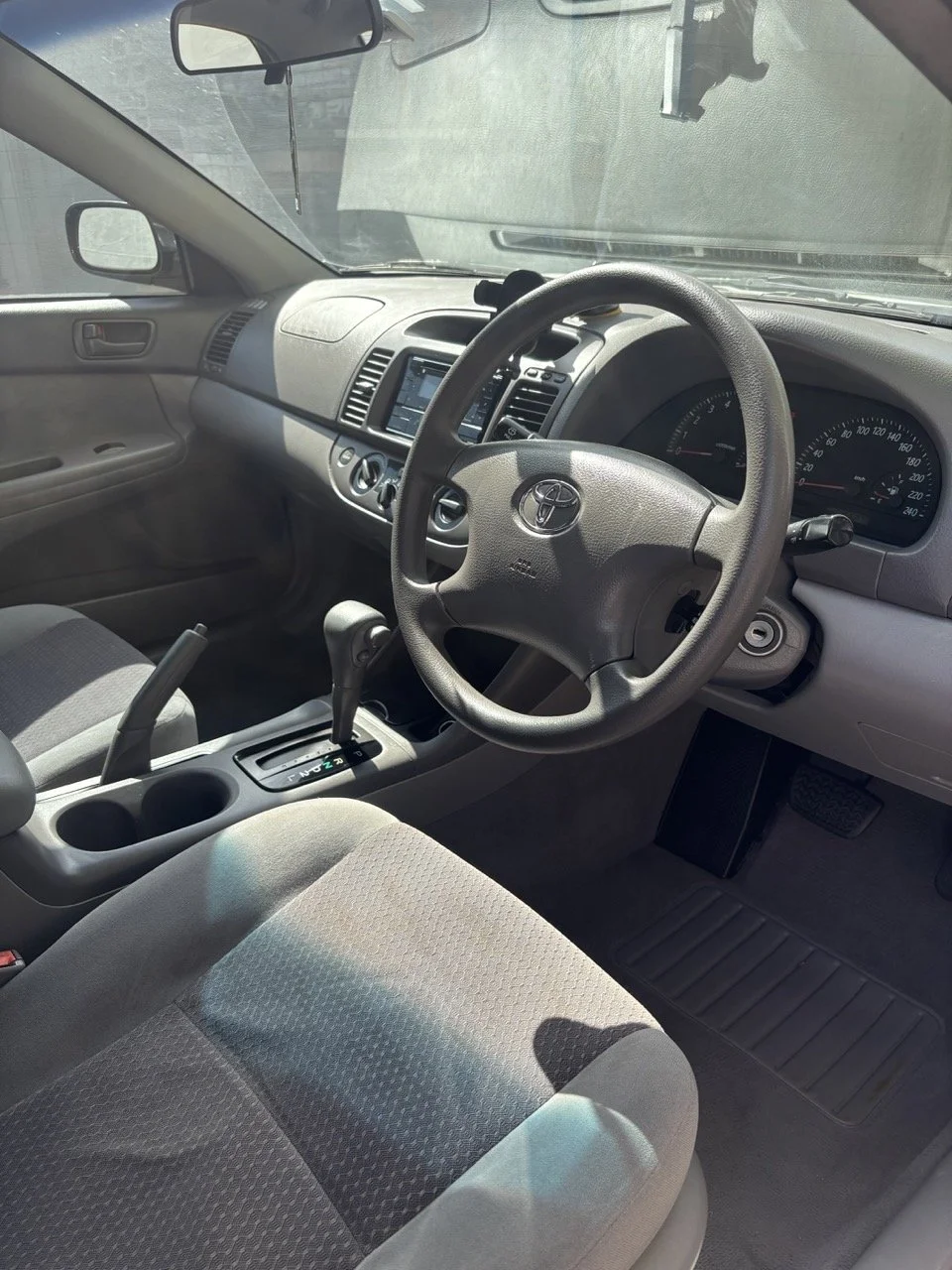 Interior of a Toyota vehicle, showing the steering wheel, dashboard, gear shift, and front seats.