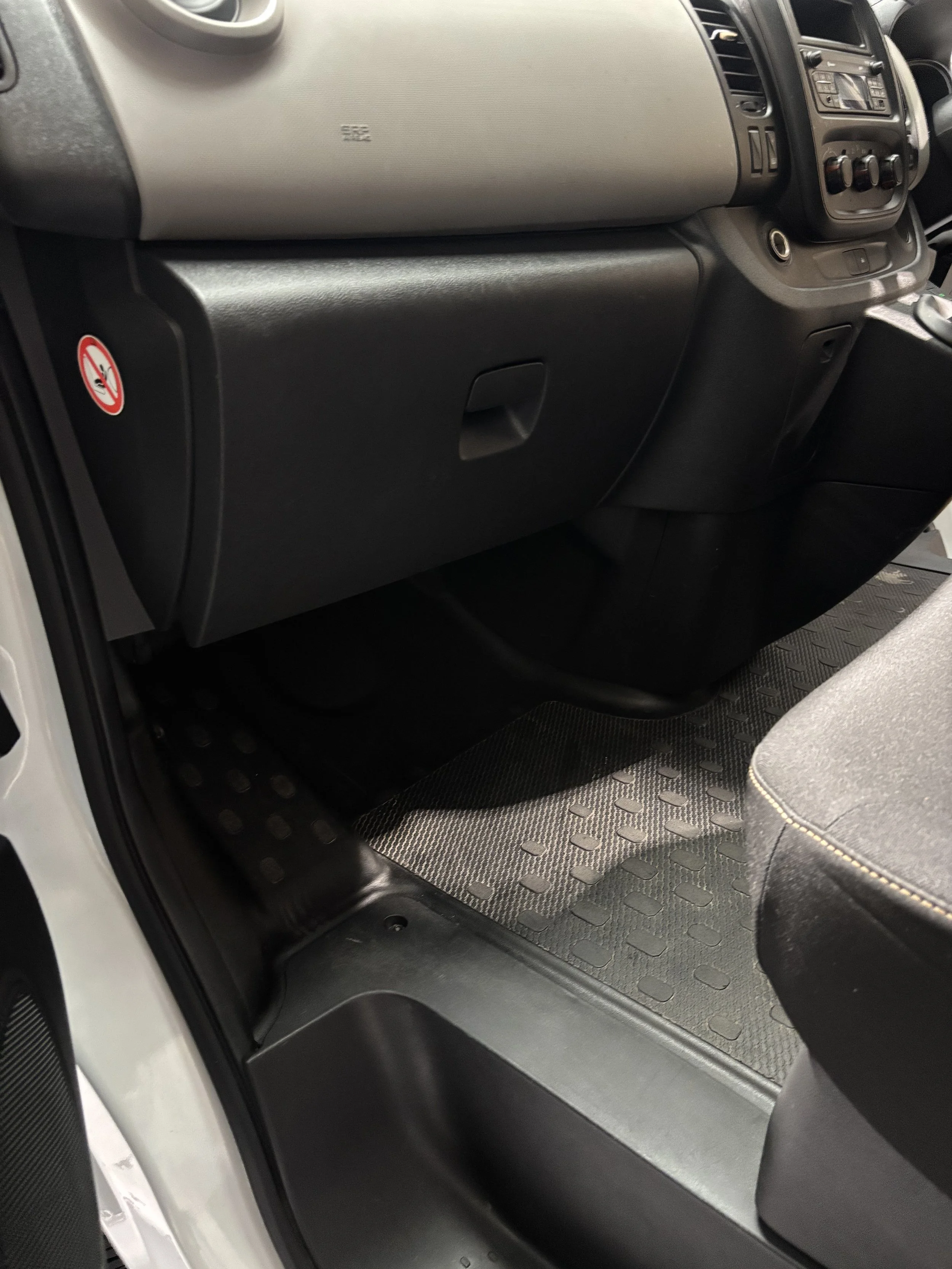 Close-up of a vehicle dashboard and front passenger footwell, with a rubber floor mat, glove compartment, and part of the seat visible.