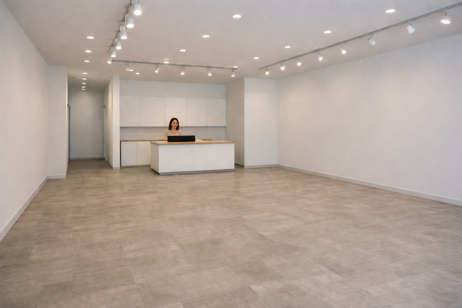 Empty retail or gallery space with a woman at a reception desk, white walls, and track lighting on the ceiling.