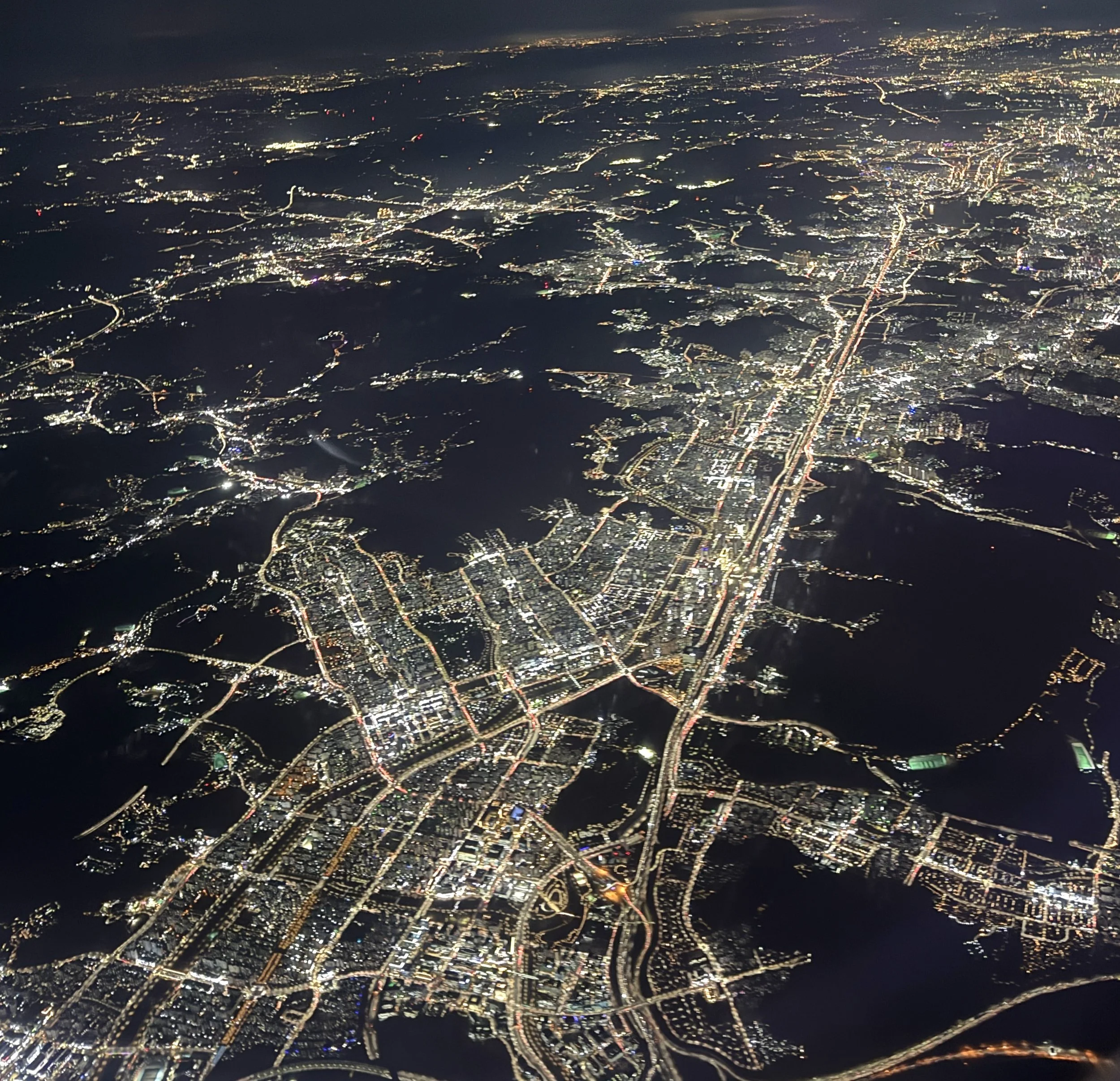 Aerial night view of a city with illuminated streets, buildings, and waterways.