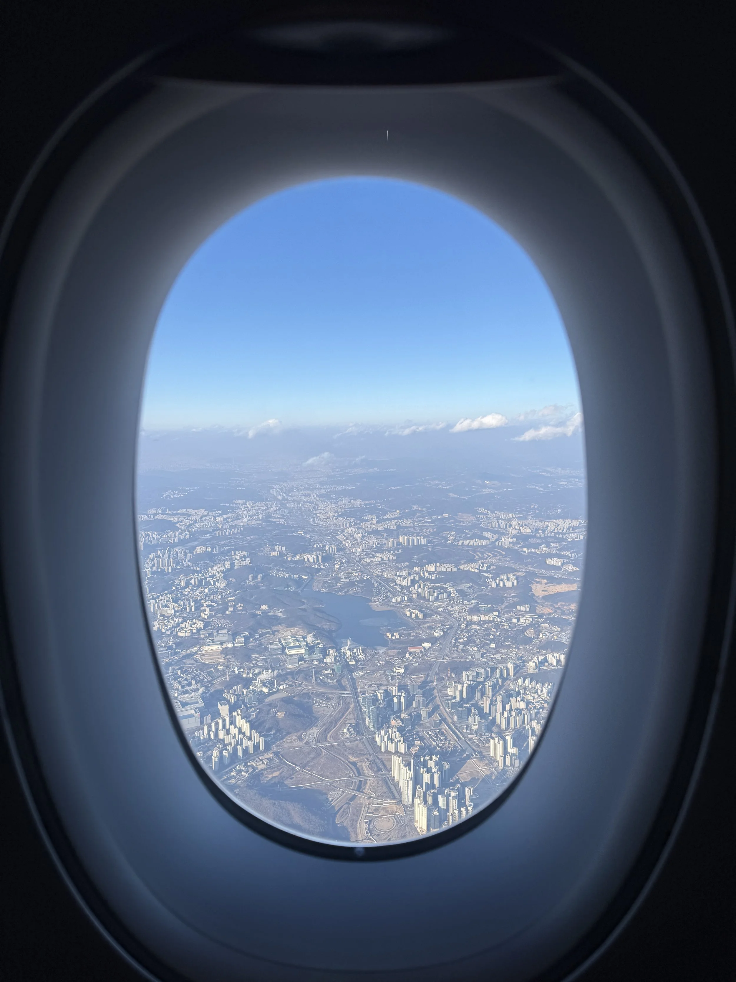 View of a cityscape with buildings, a lake, and roads seen from an airplane window.