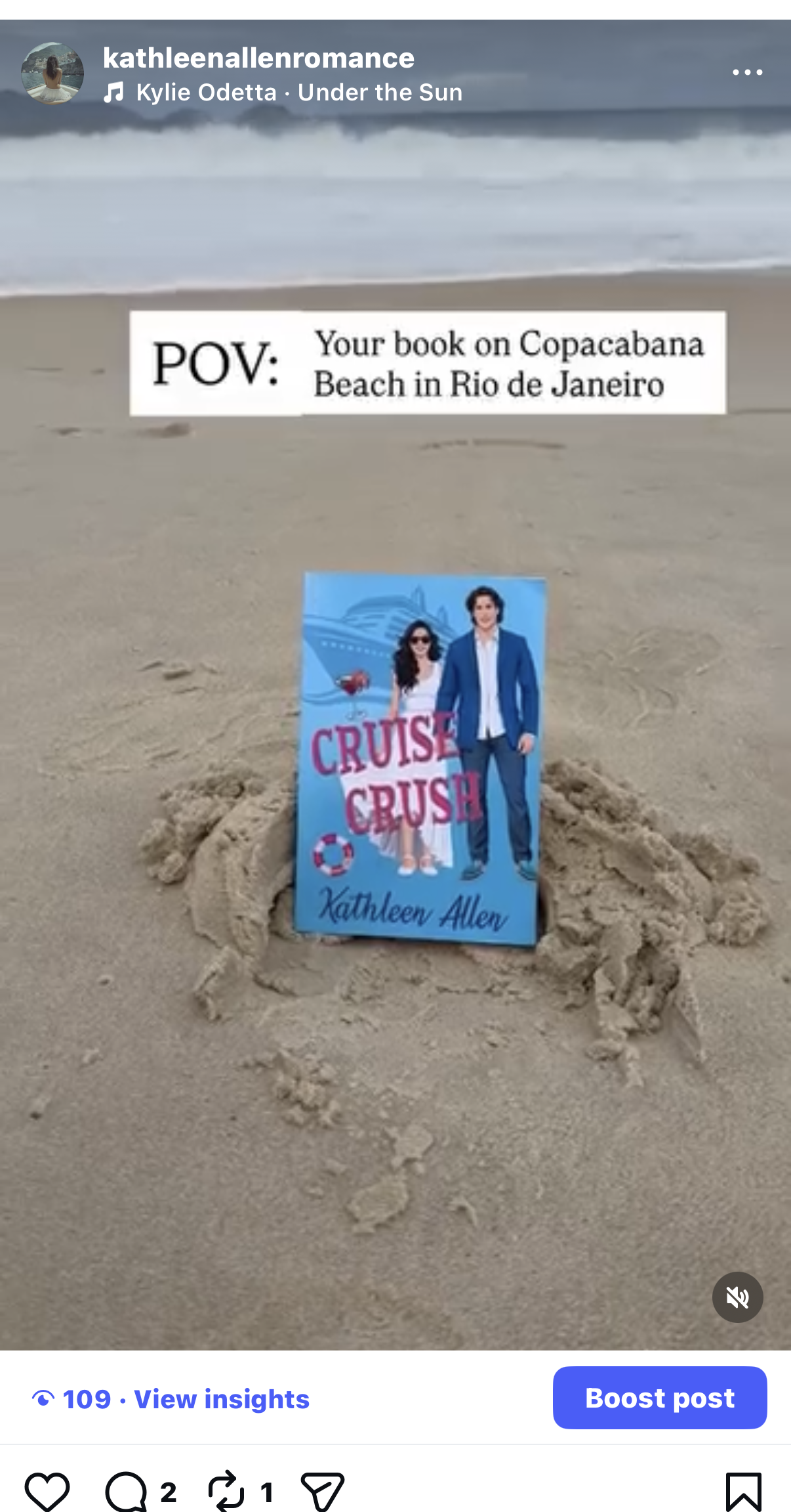 A small poster for the book 'Cruise Crush' by Kathleen Allen, placed in a hole in the sand at Copacabana Beach in Rio de Janeiro. The background shows the ocean waves.