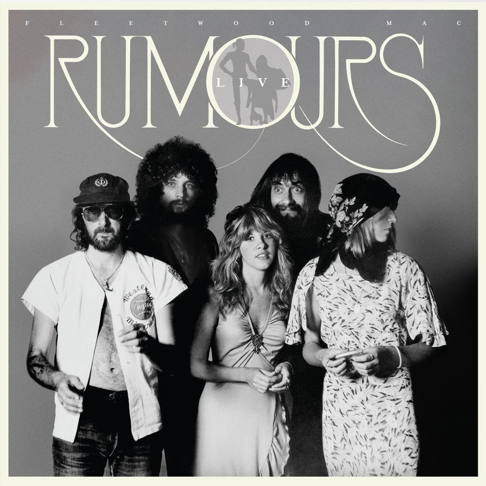 Black and white promotional photo of Fleetwood Mac's Rumours live tour featuring five band members. Two women and three men, dressed in casual 70s style clothing, are standing against a gray background with the tour and band name displayed at the top.