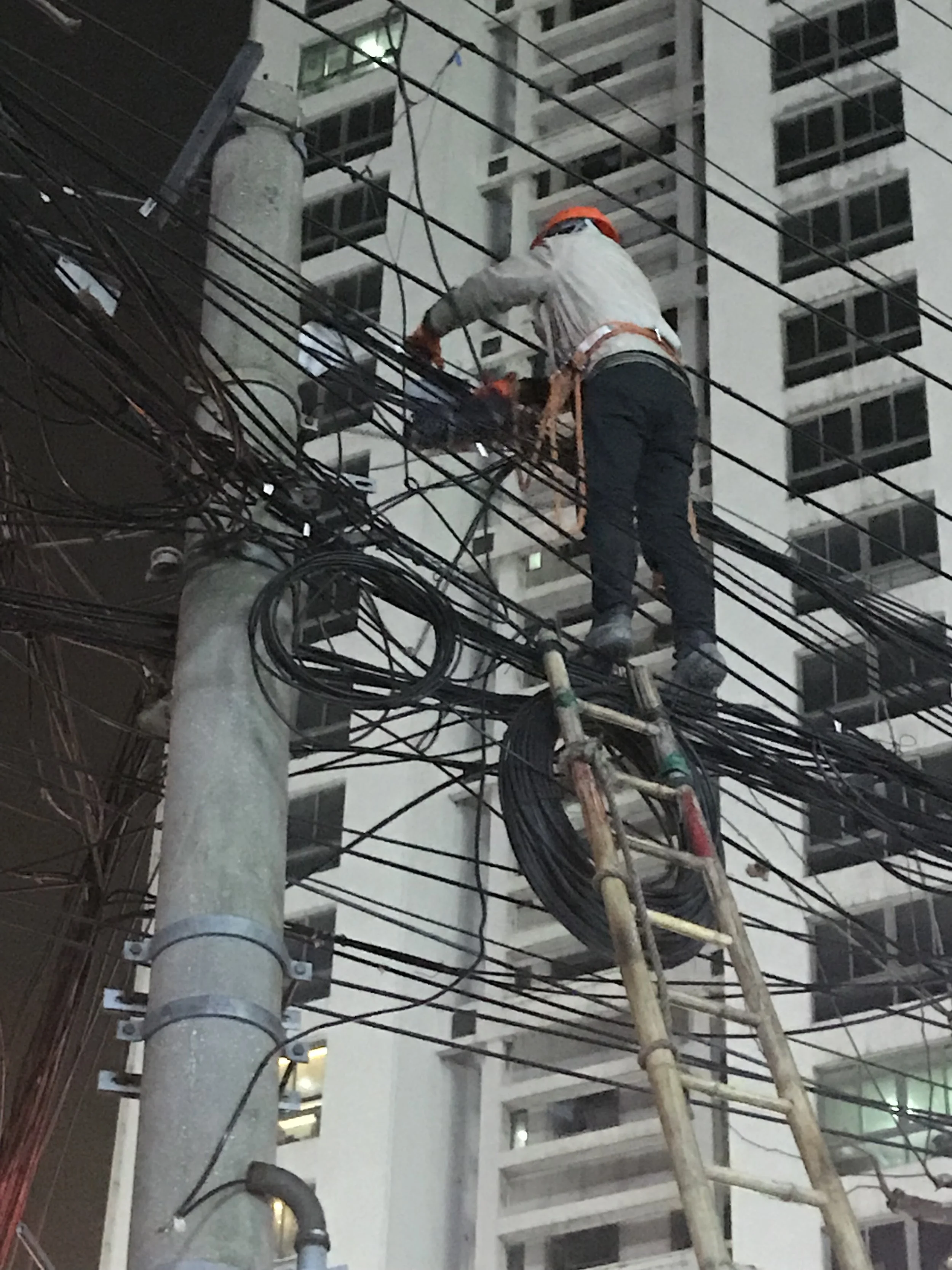 Worker on a ladder repairing electrical wires on a utility pole at night.