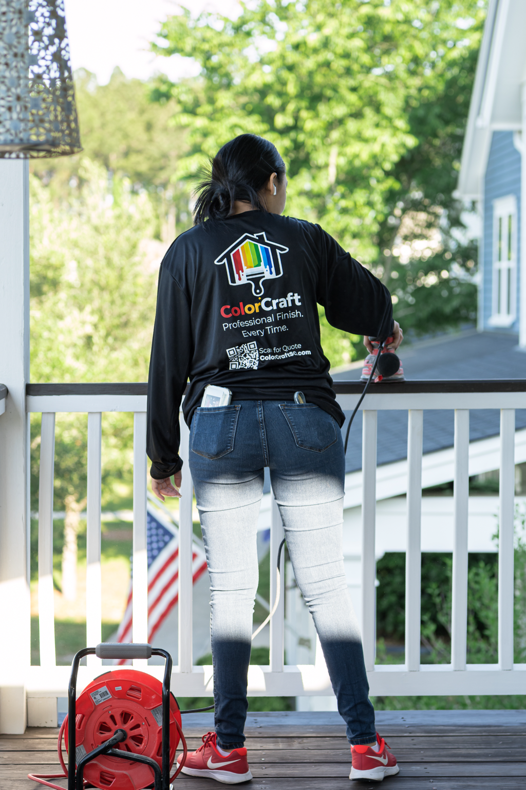 A woman wearing a black jacket with the ColorCraft logo, working on a porch with a power washer.